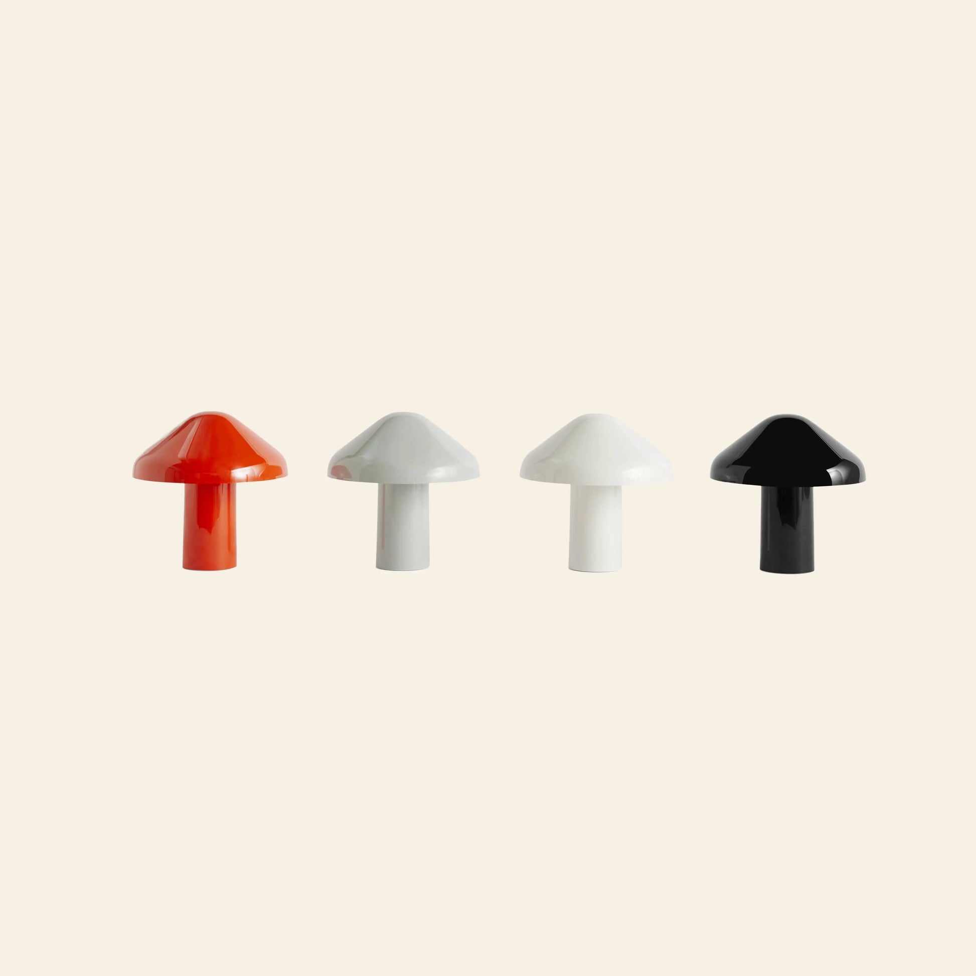 Four mushroom-shaped objects in red, light gray, white, and black stand in a row on a plain background—these are HAY Pao Portable Lamps by HAY, featuring Naoto Fukasawa’s refined minimalist and portable design.