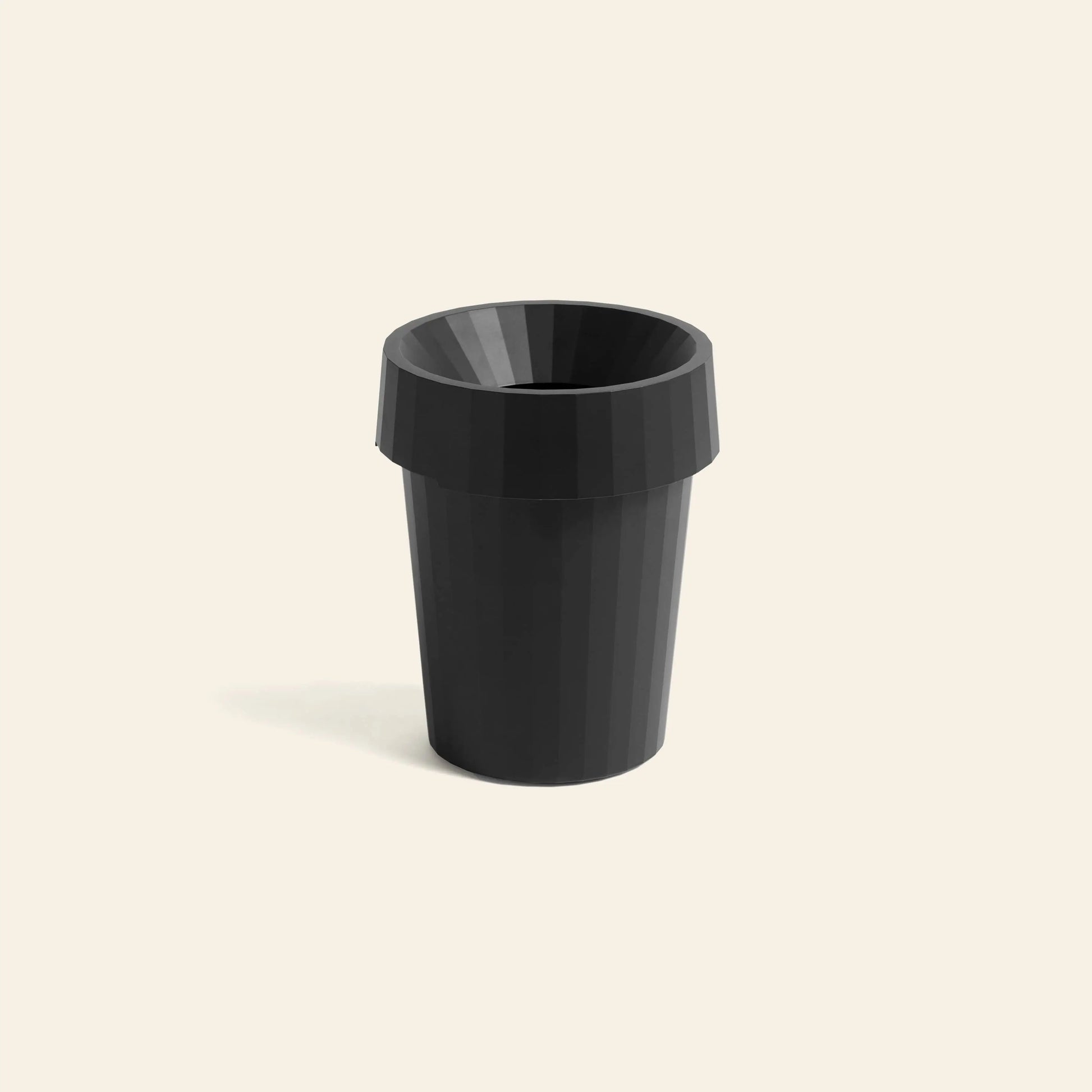 A black, ribbed HAY Shade Bin by HAY, made from durable polypropylene with a wide, flared rim, stands centered on a plain light beige background.