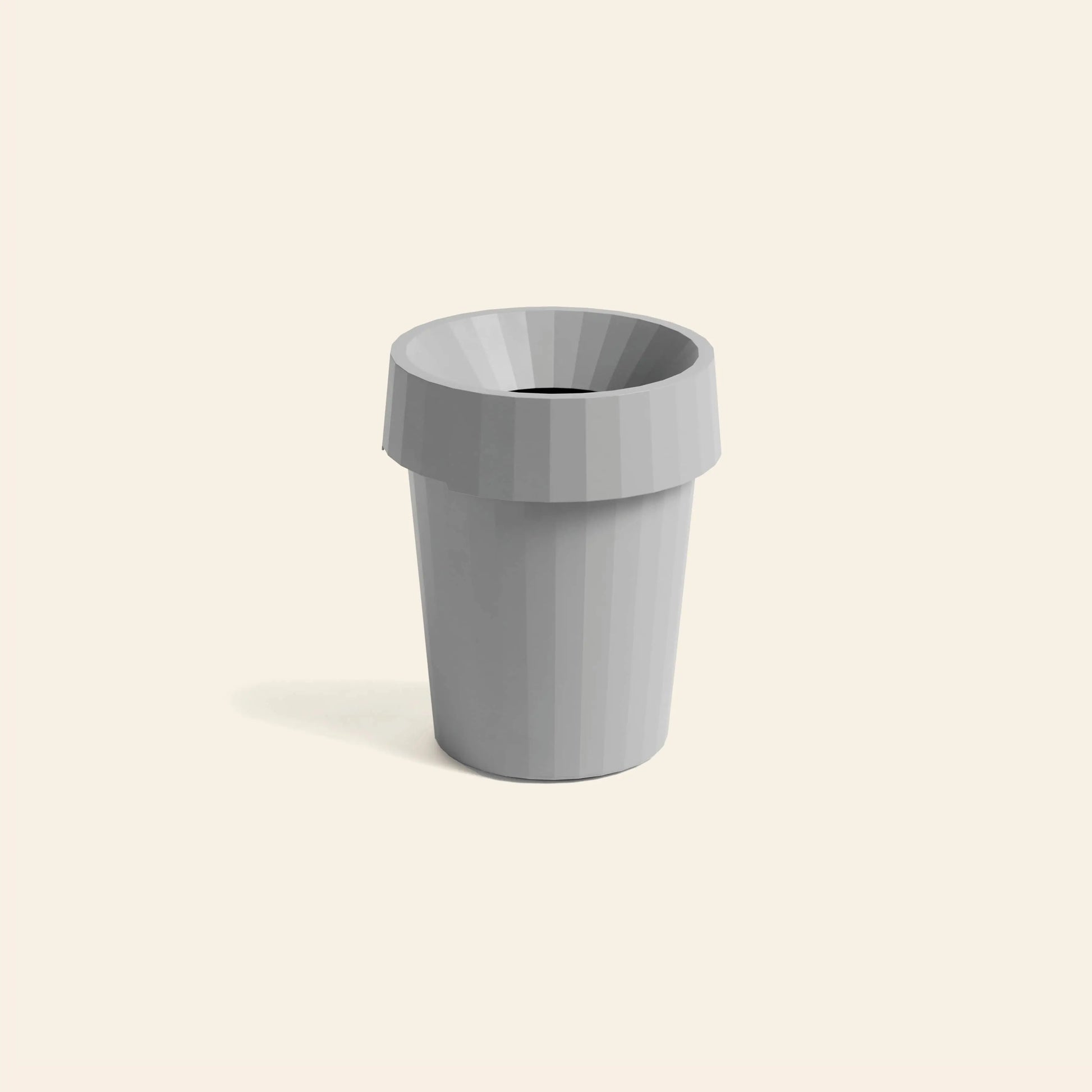 The HAY Shade Bin by HAY is a gray, faceted polypropylene cylinder with a wide, angled rim—a modern minimalist design ideal for spaces with muted tones. Shown on a light beige background.
