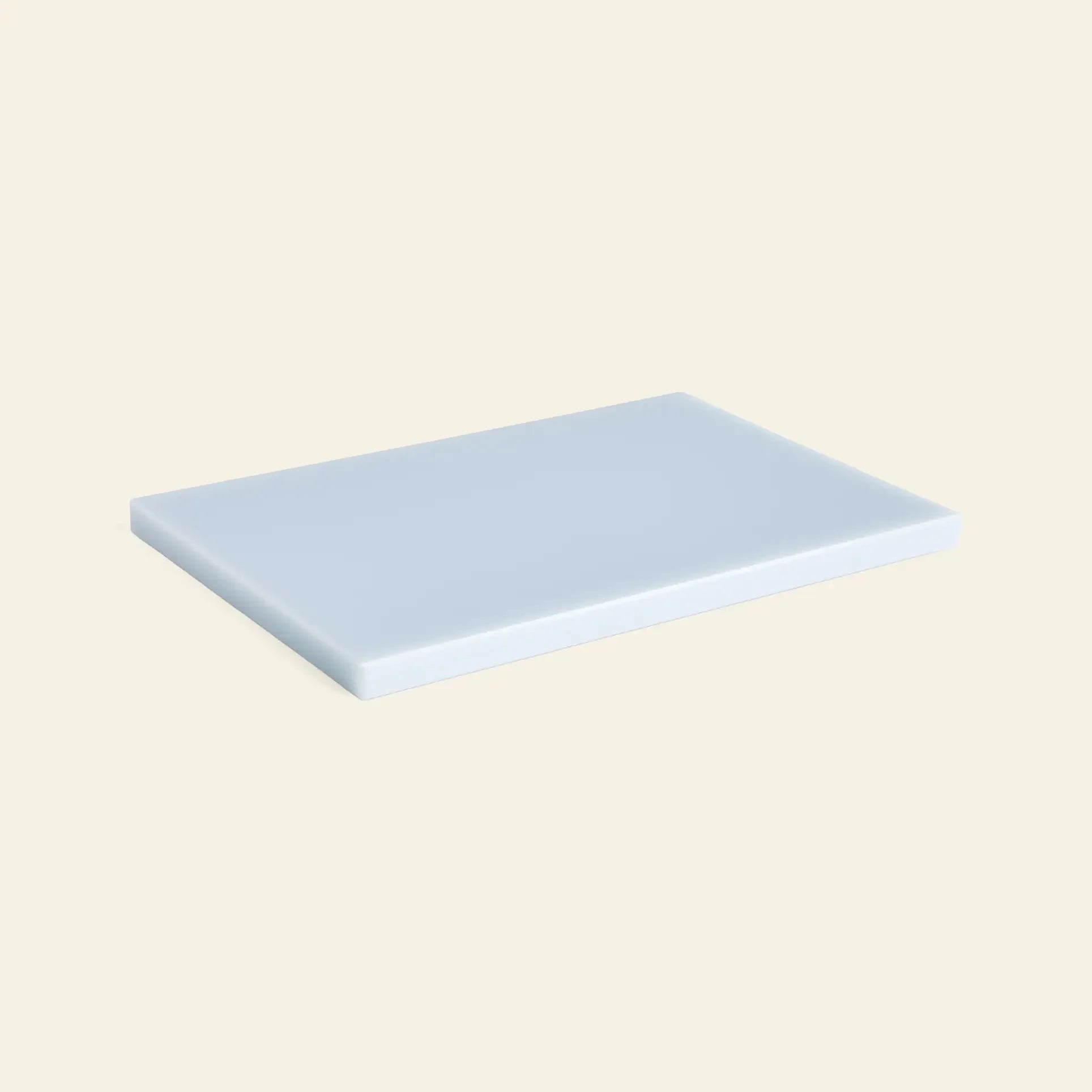 The HAY Slice Chopping Board L by HAY, in light blue with smooth edges, sits on a beige background—an ideal rectangular kitchen essential to help prevent cross-contamination.