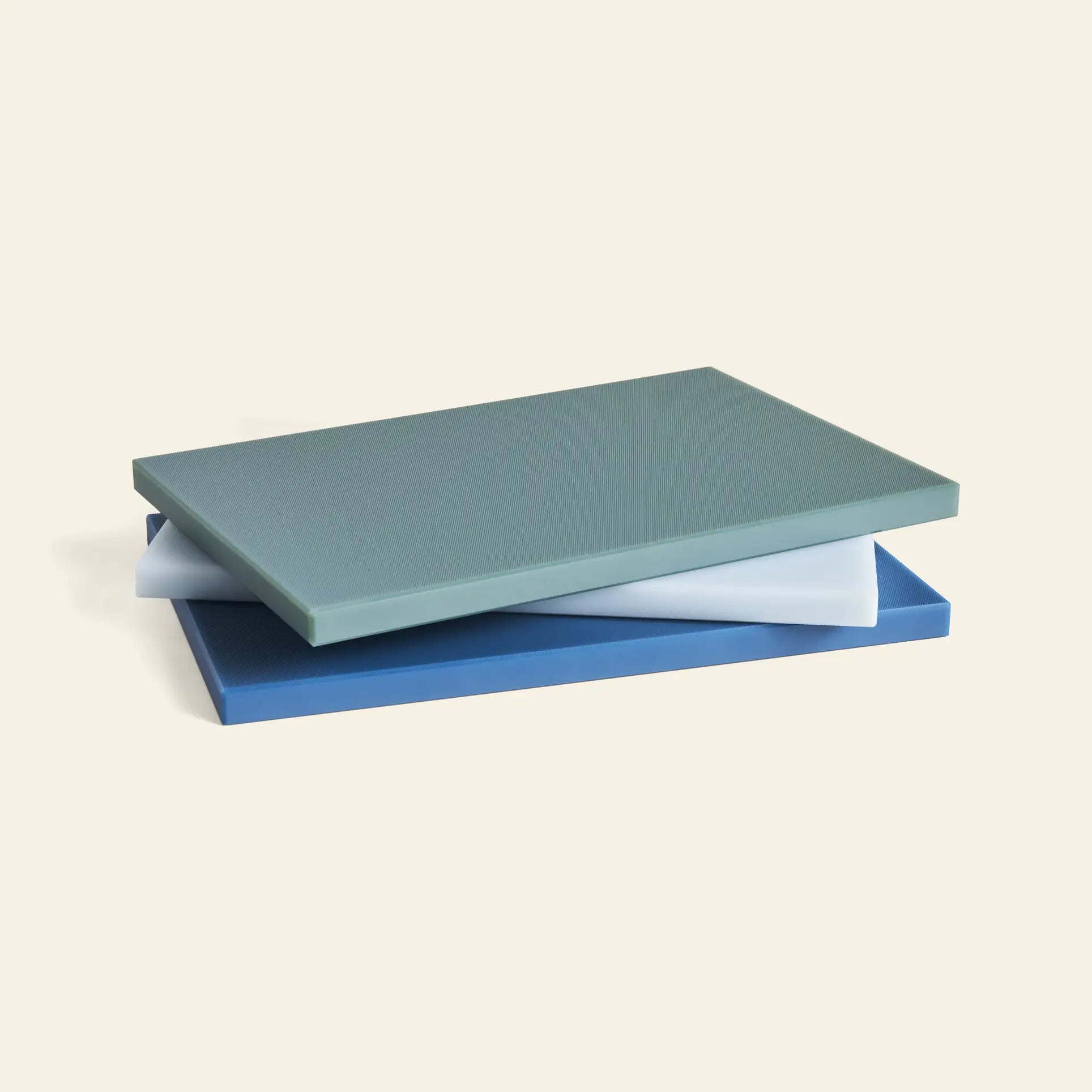 Three HAY Slice Chopping Board L in green, white, and blue by HAY are stacked slightly askew against a plain light background—ideal kitchen essentials for helping prevent cross-contamination.