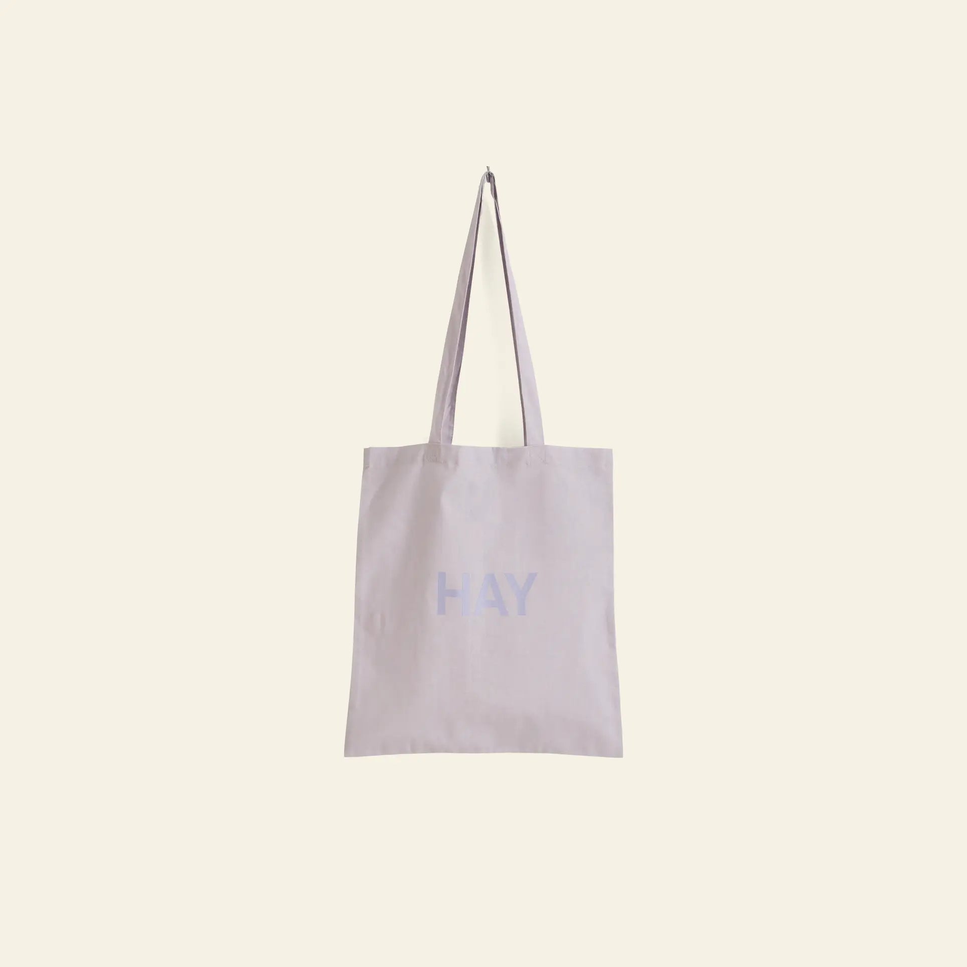 The HAY Tote Bag by HAY is made from organic cotton and features two long handles. This OEKO-TEX® STANDARD 100 certified beige bag has HAY printed in light blue on the front and is shown against a light cream background.