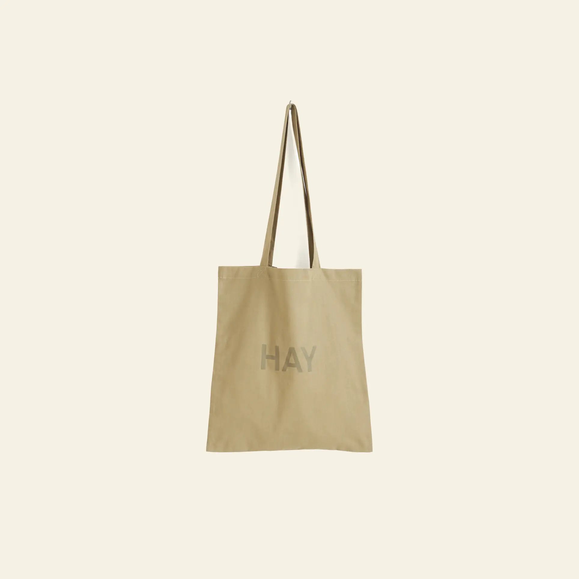 The HAY Tote Bag by HAY is made from organic cotton in beige, featuring long handles and a light gray HAY print on the front. Shown on an off-white background. OEKO-TEX® STANDARD 100 certified for peace of mind.