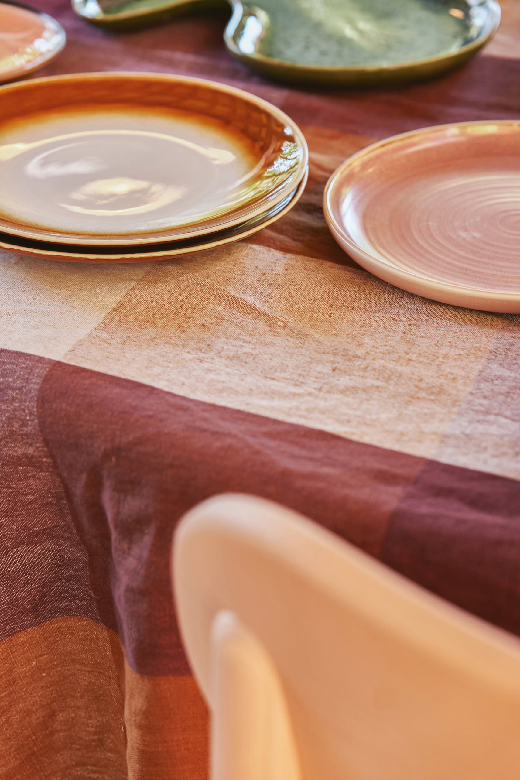 A close-up of a table set with HKLIVING 70s Ceramics: Dinner Plates, Set of 2 - Supernova, featuring hand-glazed finishes in warm tones on a brown and mauve checkered tablecloth, with a light chair partly visible.