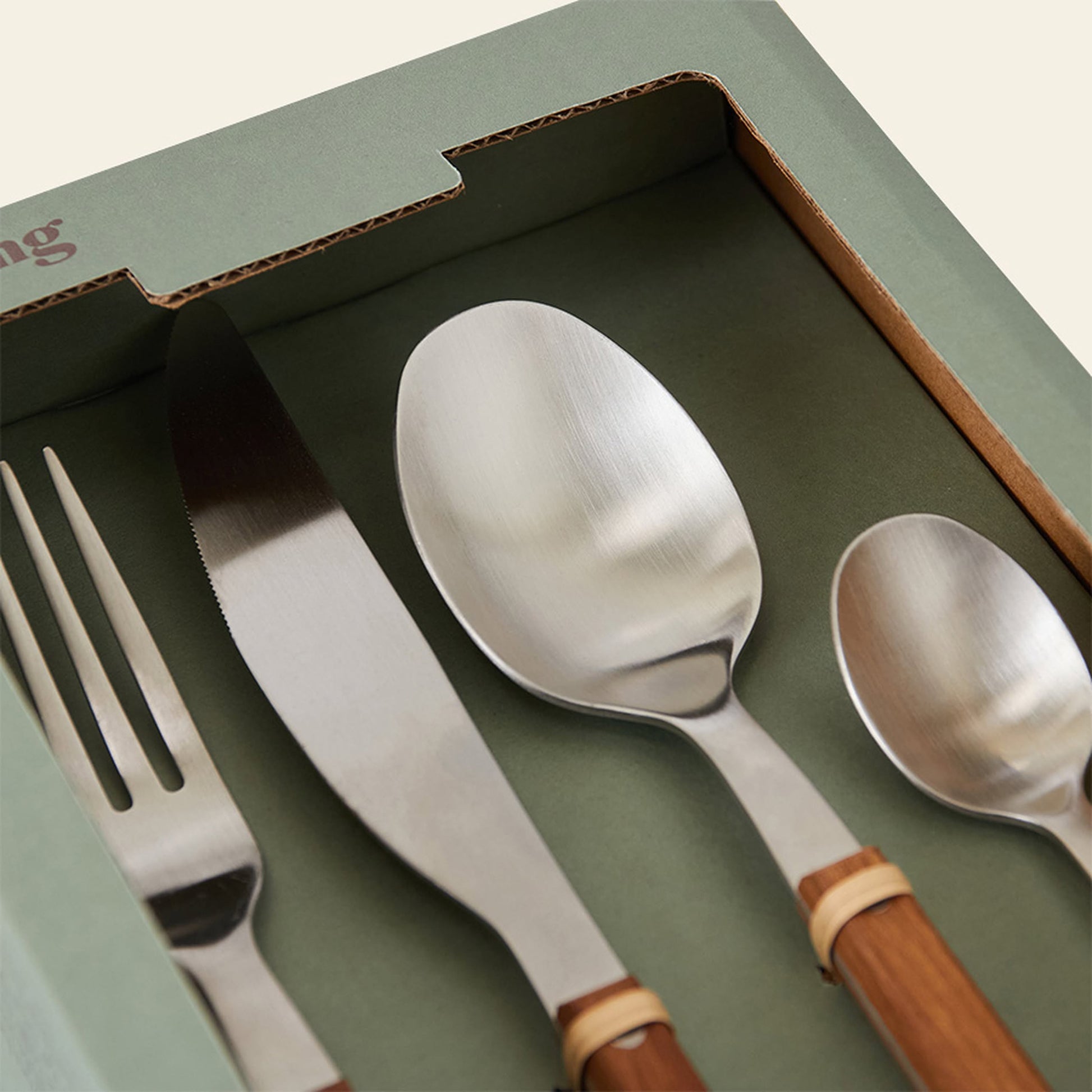 A close-up of the HKLIVING 70s Cutlery: Wood, Set of 16 by HKLIVING shows metal utensils with brown wooden handles, including fork, knife, and spoons, beautifully arranged against a green background.