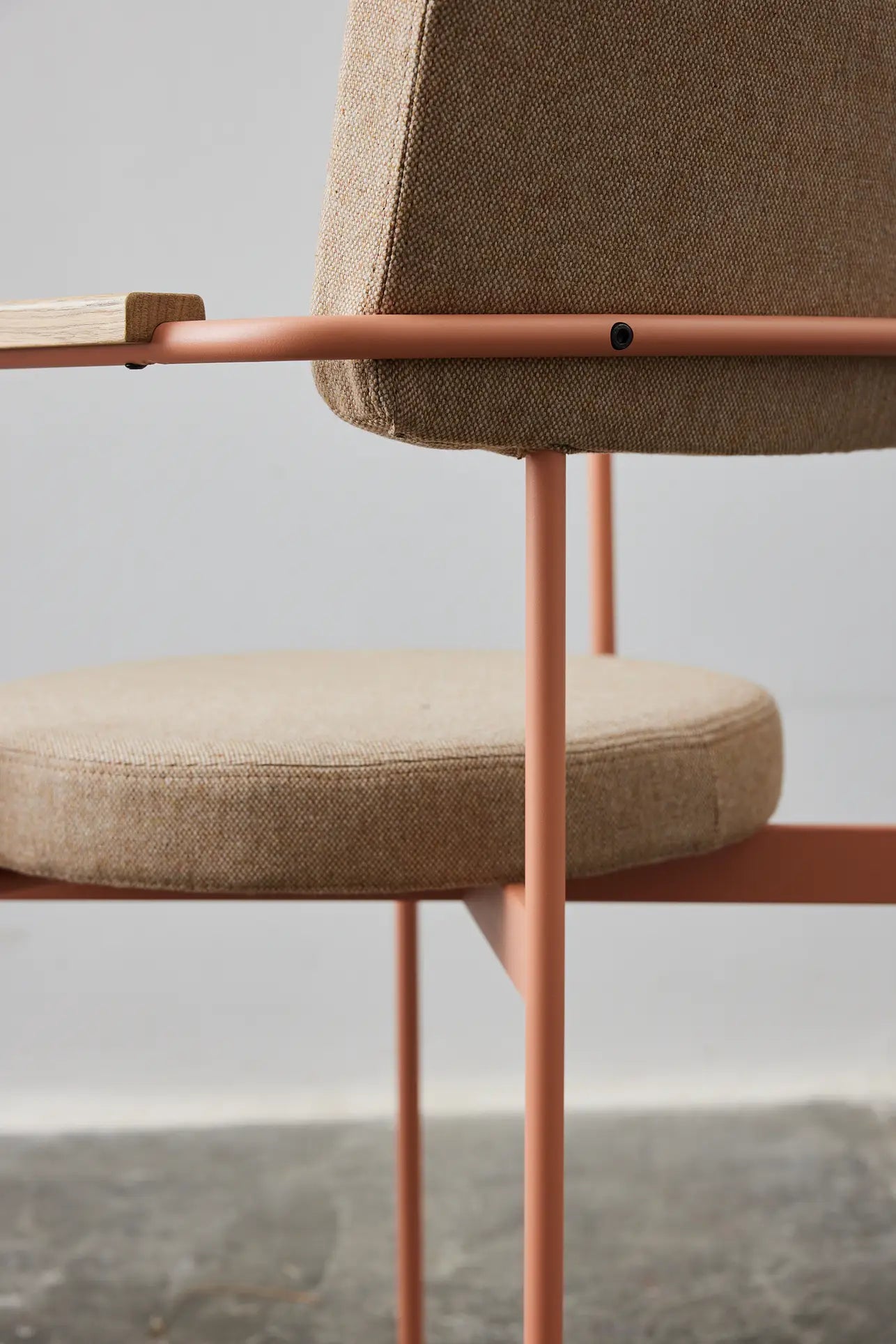 A close-up of the HKliving Dining Armchair, Main Line Flax, Nude by HKliving features a beige upholstered seat and backrest with a pink metal frame, set against a neutral background and concrete floor.