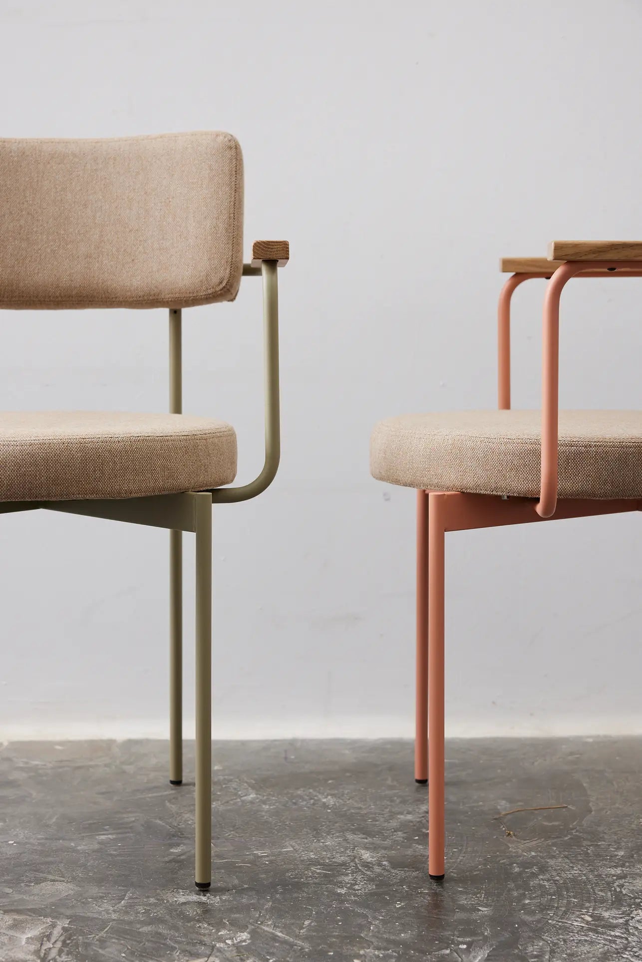 The HKliving Dining Armchair, Main Line Flax, Nude features a minimalist Dutch design with stackable metal legs and beige cushions—stylish, customizable seating in soft nude tones from brand HKliving. Perfect against a gray wall and concrete floor.