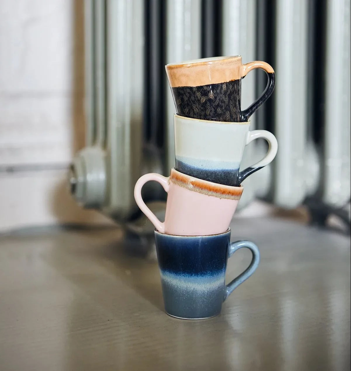 Four HKliving 70s Ceramics Espresso Mugs (80ml each) in assorted colors are stacked on a smooth surface, with a softly blurred background—perfect for ceramic lovers. Set of 4 by HKliving.