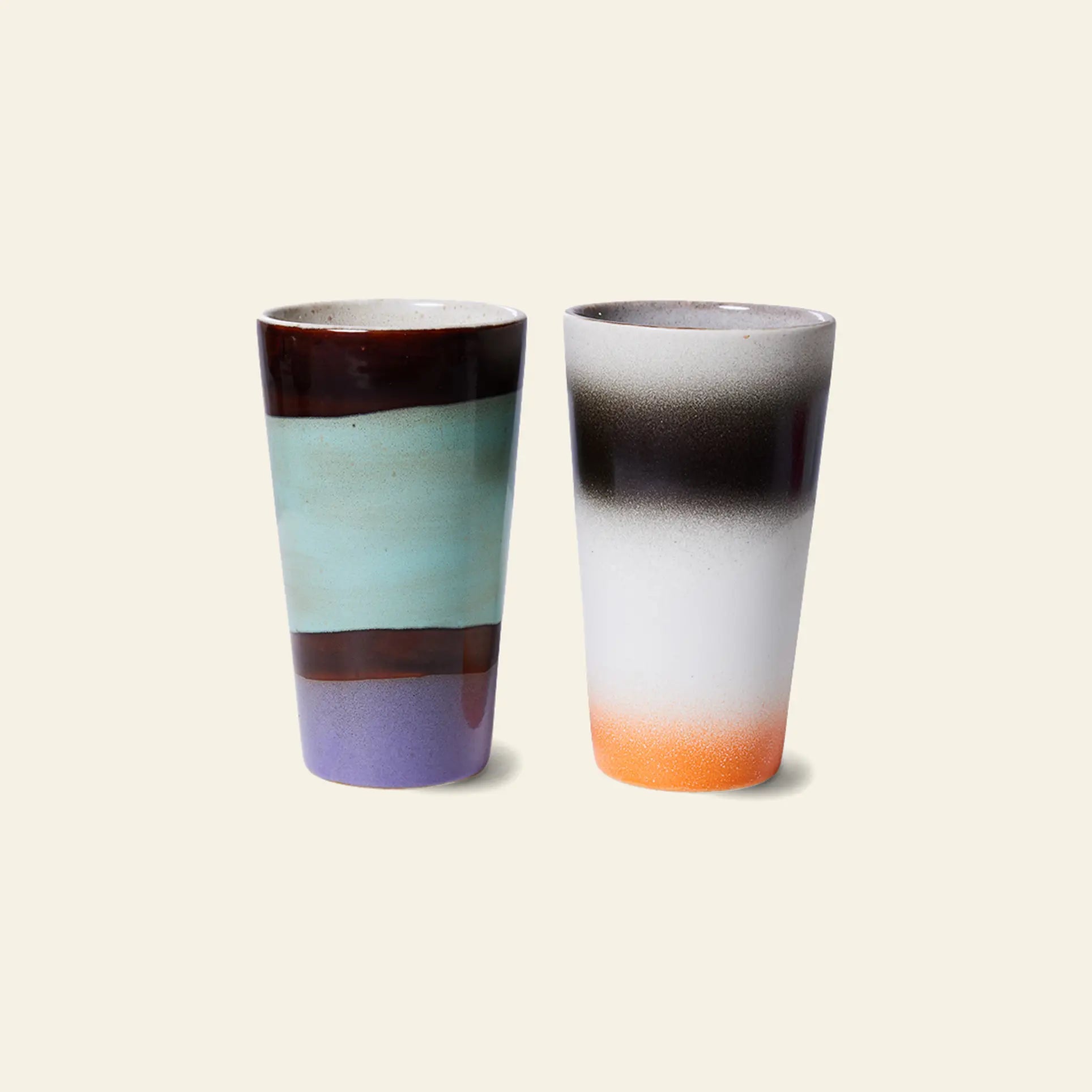 The HKliving 70s Ceramics: Latte Mugs Set of 2 features tall ceramic mugs—one with brown, turquoise, and purple bands, the other with a black-to-white-to-orange gradient—perfect for your morning latte or espresso.
