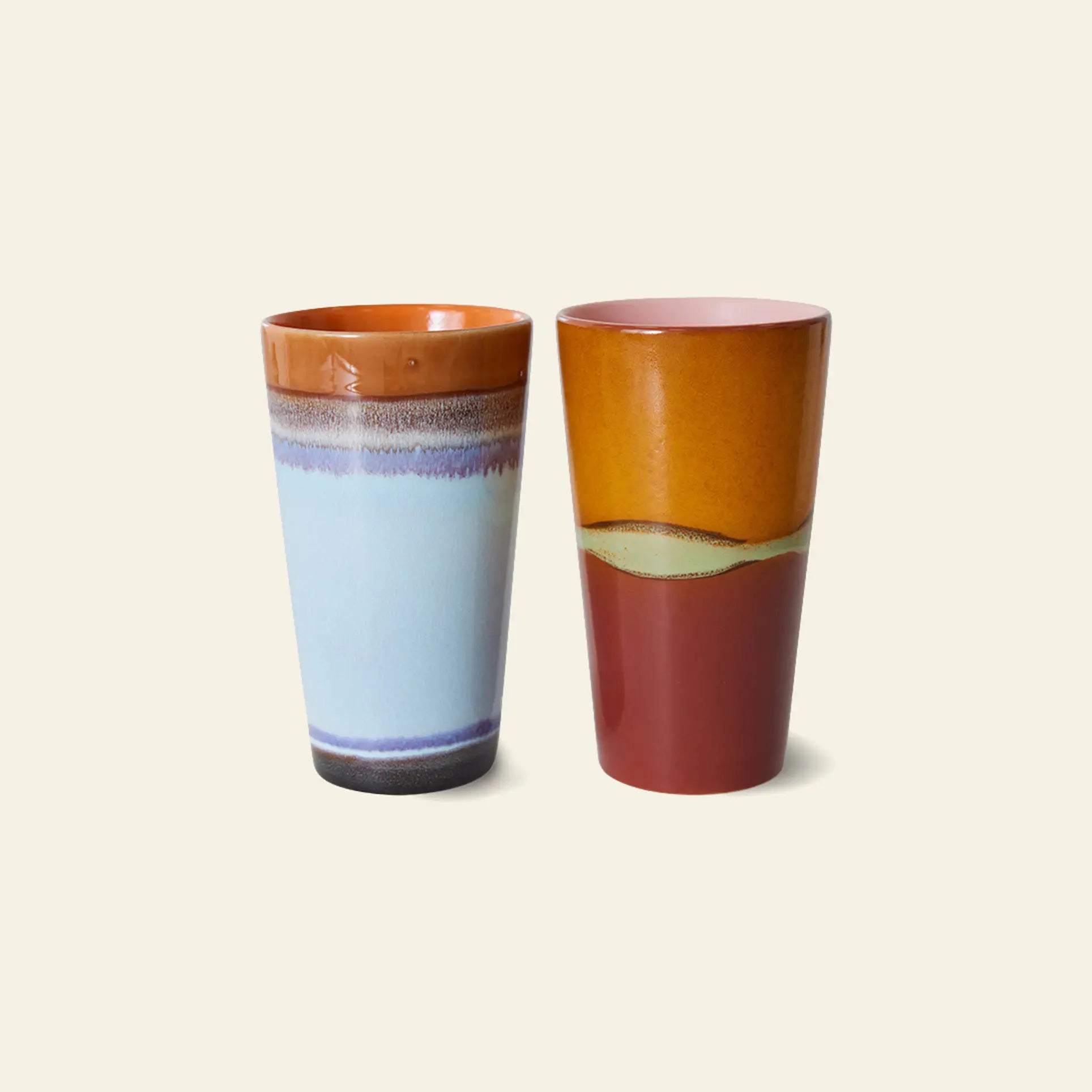 The HKliving 70s Ceramics: Latte Mugs (set of 2) feature tall, glossy designs—one in light blue with a brown rim/base, the other reddish-orange with mustard yellow and green accents—perfect for lattes or espresso.
