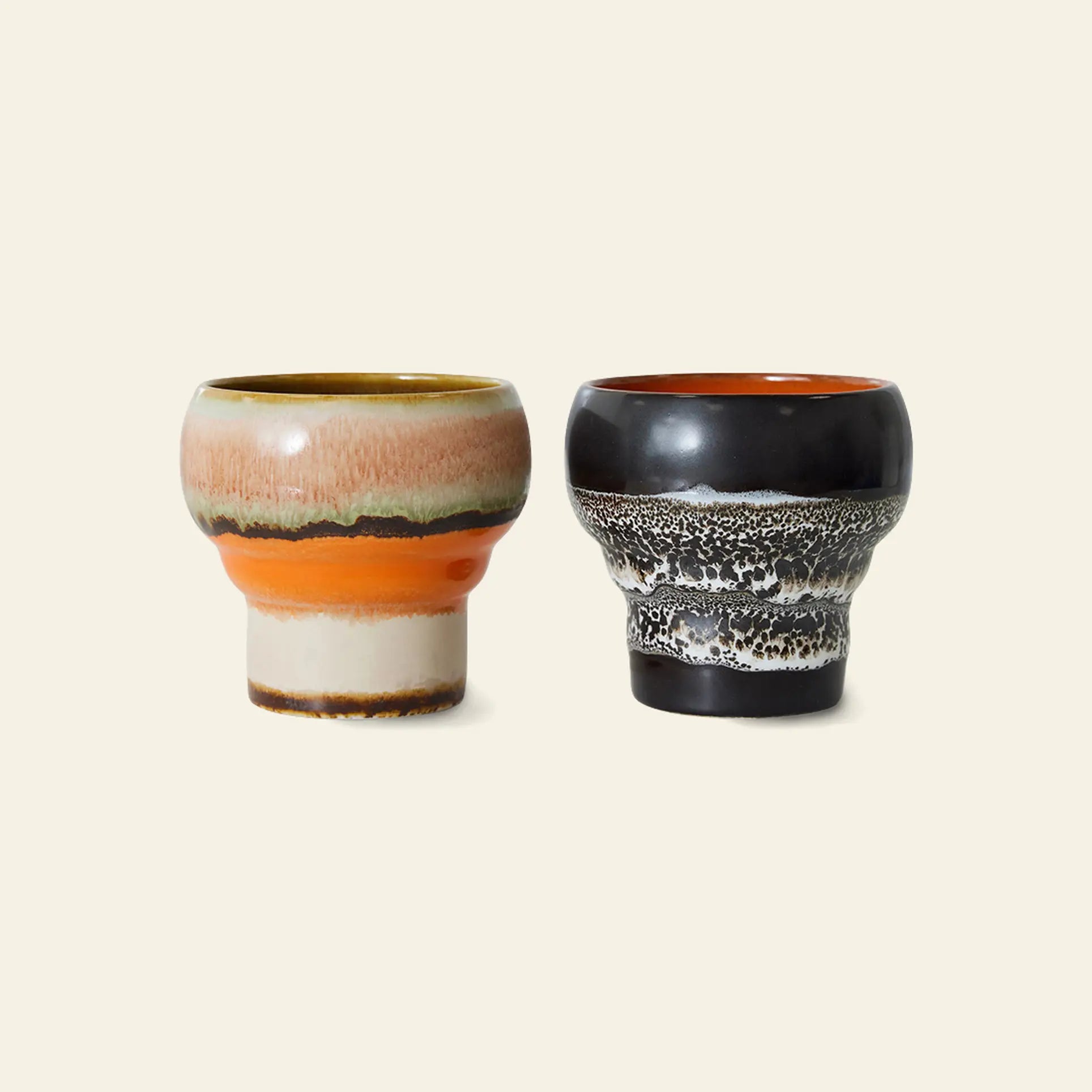 The HKLIVING 70s Ceramics: Lungo Mugs, Set of 2 features one mug with orange, beige, and brown layers and another with a black-gray textured pattern and glossy orange interior—perfect for coffee lovers.