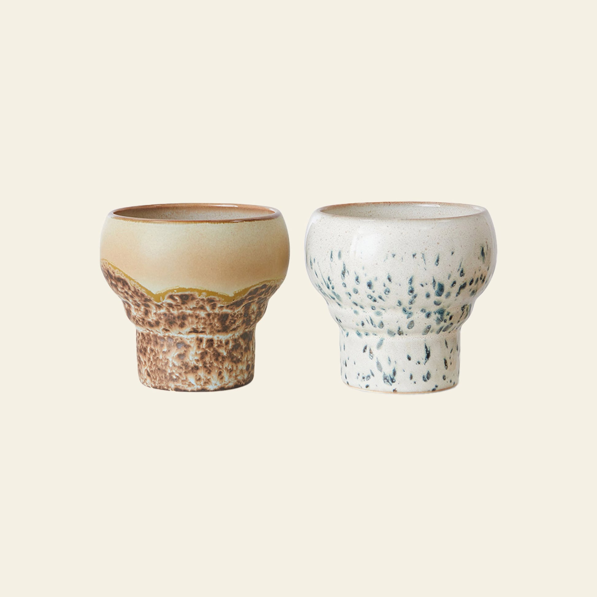 The HKLIVING 70s Ceramics: Lungo Mugs Set of 2 features a brown mug with a textured base and yellow top, and an off-white mug with dark speckles—perfect for coffee lovers, both displayed on a plain light background.