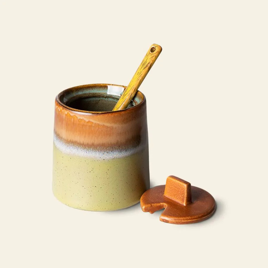 The HKliving 70s Ceramics: Milk Jug & Sugar Pot by HKliving features an earthy two-tone glaze, a matching lid, and a wooden spoon. Its glossy brown and beige finish evokes the warmth of classic 70s ceramics.