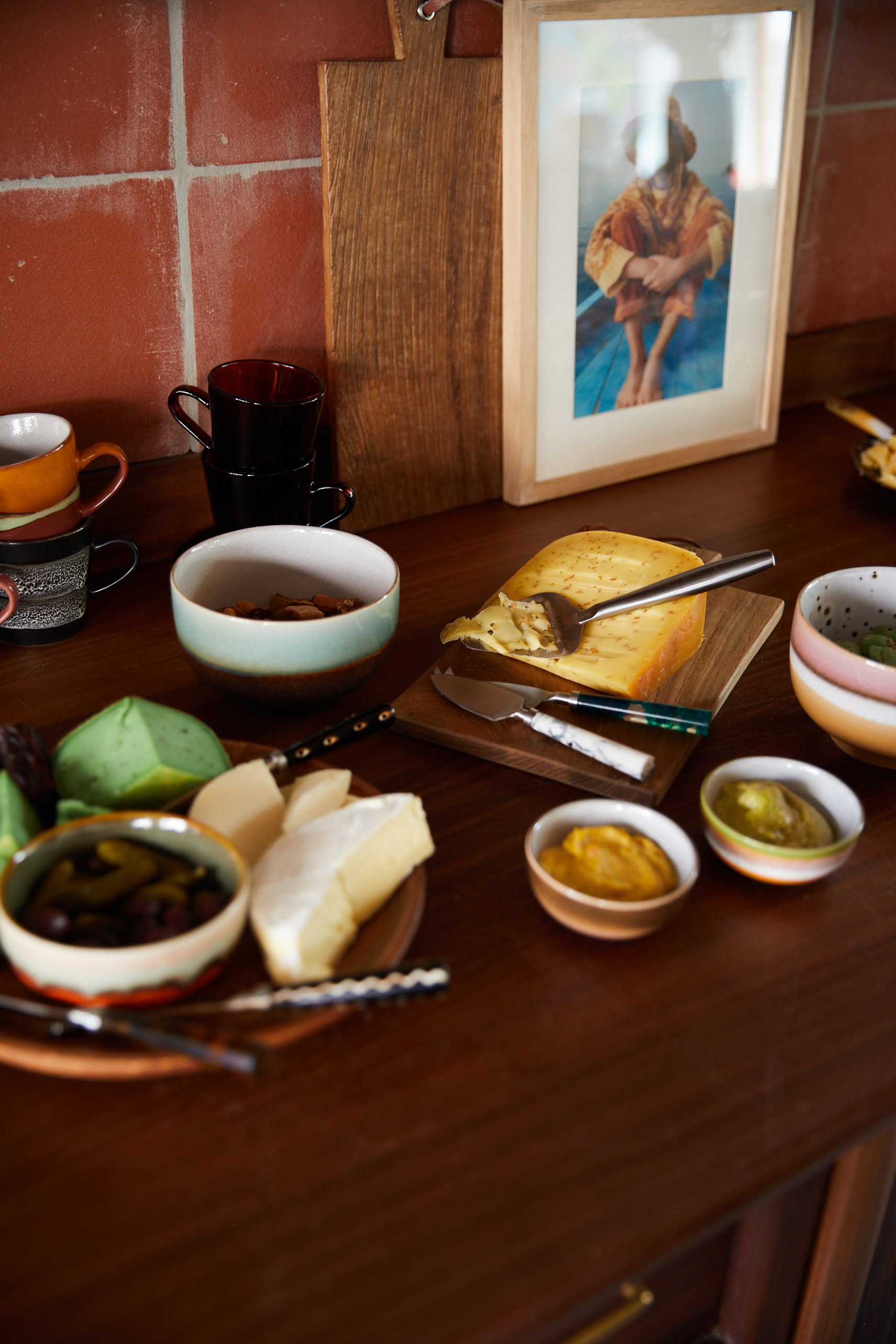 A wooden table is set with cheeses, spreads, pickles, and nuts. In the background, HKliving 70s Ceramics Noodle Bowls (Set of 4) add retro flair—perfect for serving your favorite dishes in style.