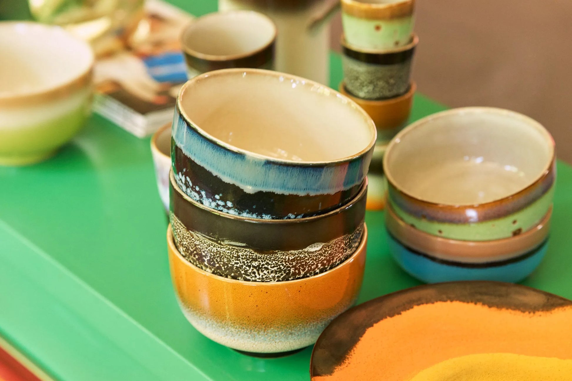 A set of four colorful HKliving 70s Ceramics Noodle Bowls sits on a bright green table, their unique patterns and glazes perfect for serving your favorite dishes.