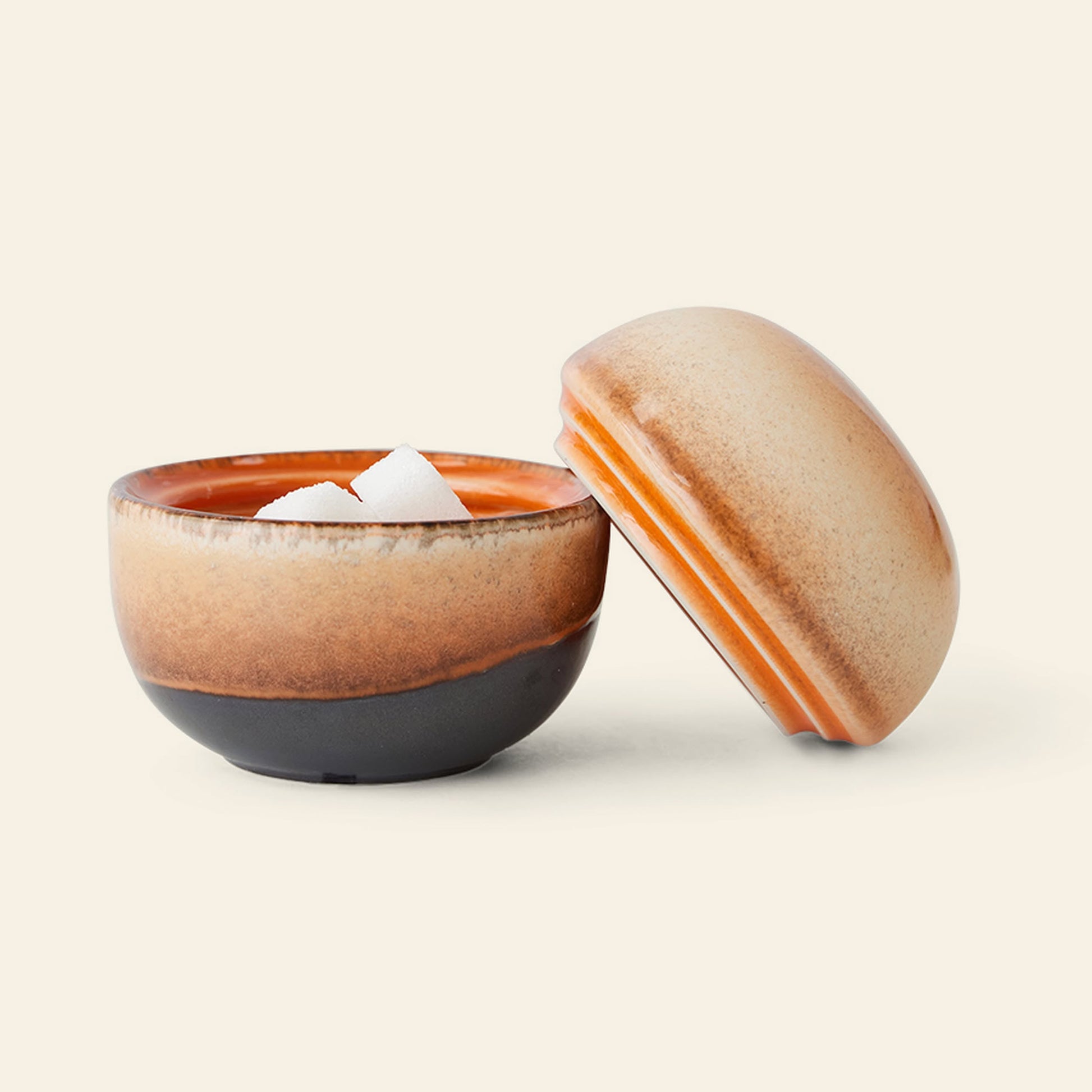 The HKliving 70s Ceramics: Sugar Pot features a round design with a brown and orange gradient glaze. With its lid set aside, it’s perfect for storing sugar cubes, condiments, or sweet treats.