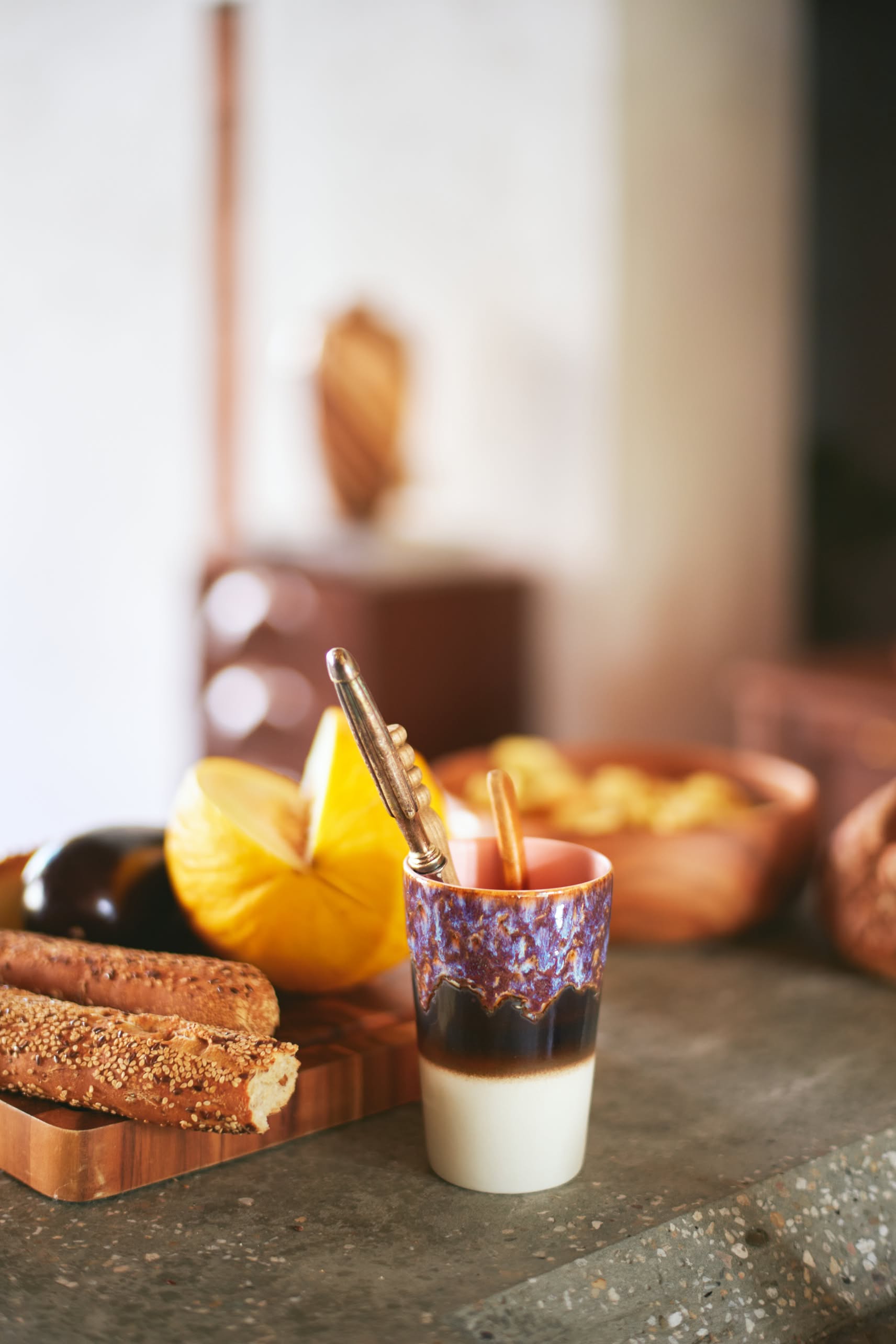 The HKliving 70s Ceramics: Tea Mugs, Set of 2 stand on the counter with sliced melon, eggplant, breadsticks, and chips in a wooden bowl, bringing a unique retro flair to the warmly lit kitchen.
