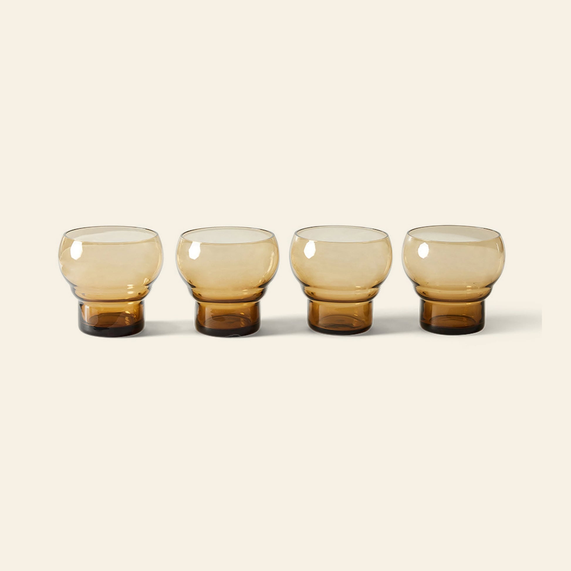 Four HKliving 70s Glassware: Bulb Glasses, Set of 4 in amber, each with a thick base, are displayed in a row on a neutral background, showcasing the brand’s retro style and sophistication.