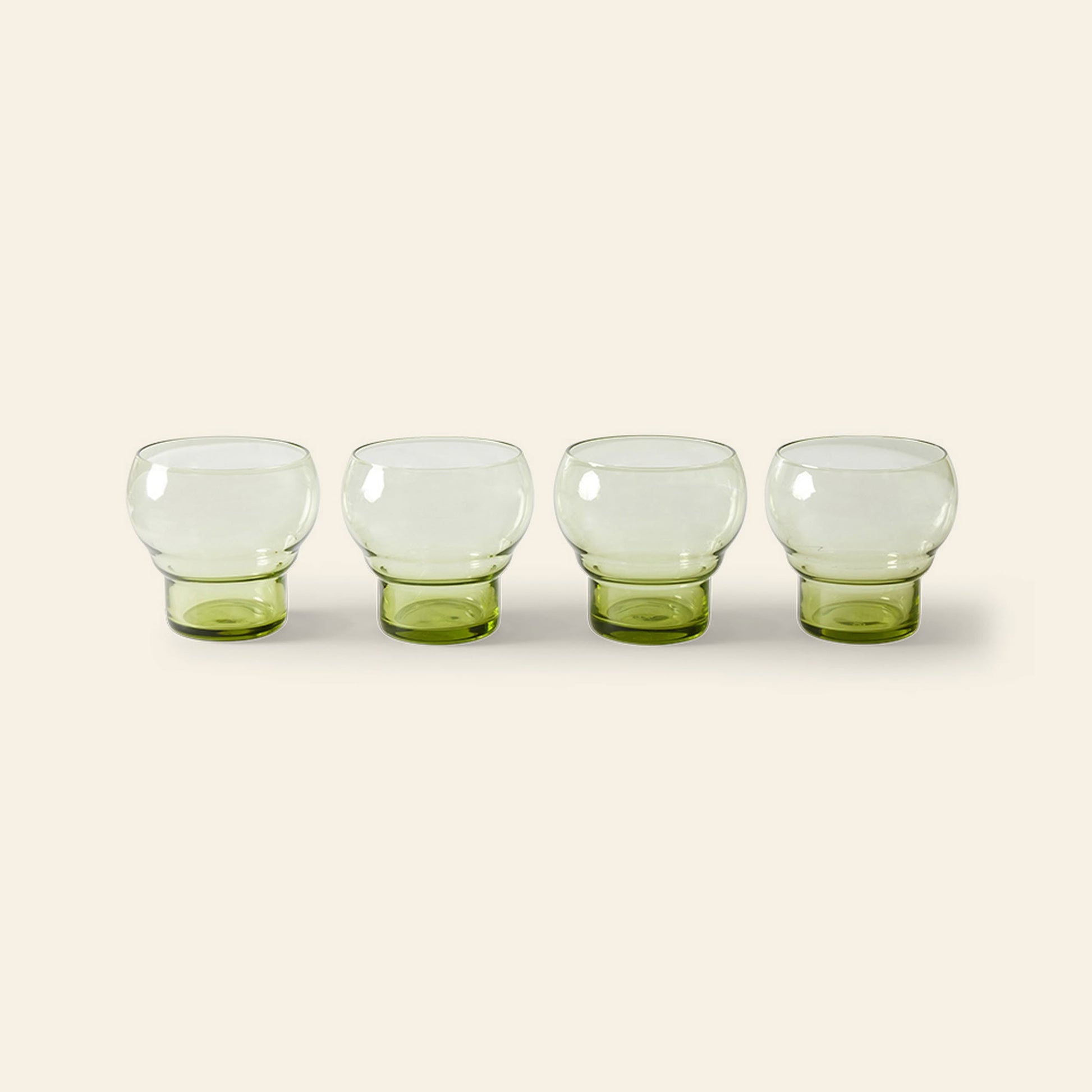Four HKliving 70s Glassware Bulb Glasses, set of 4, featuring a green tint, are lined up side by side on a light beige background, bringing retro sophistication from HKliving to your table.