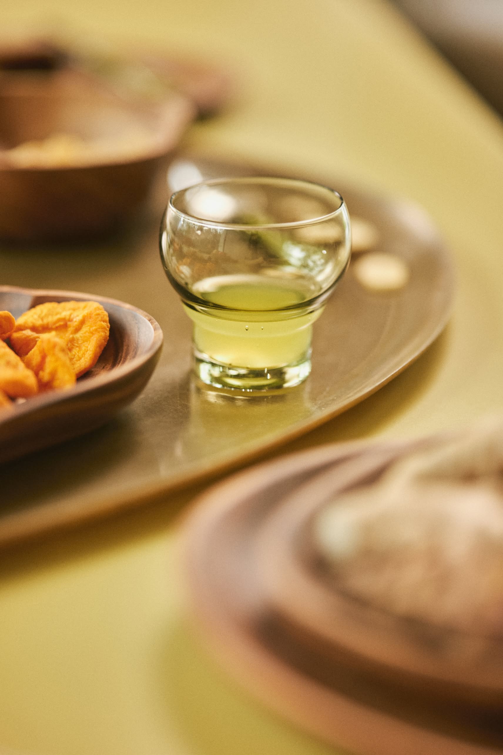 The HKliving 70s Glassware: Bulb Glasses, Set of 4, with their light green hue, add a retro touch and sophistication when placed on a tray beside wooden dishes filled with snacks in this softly focused table scene.