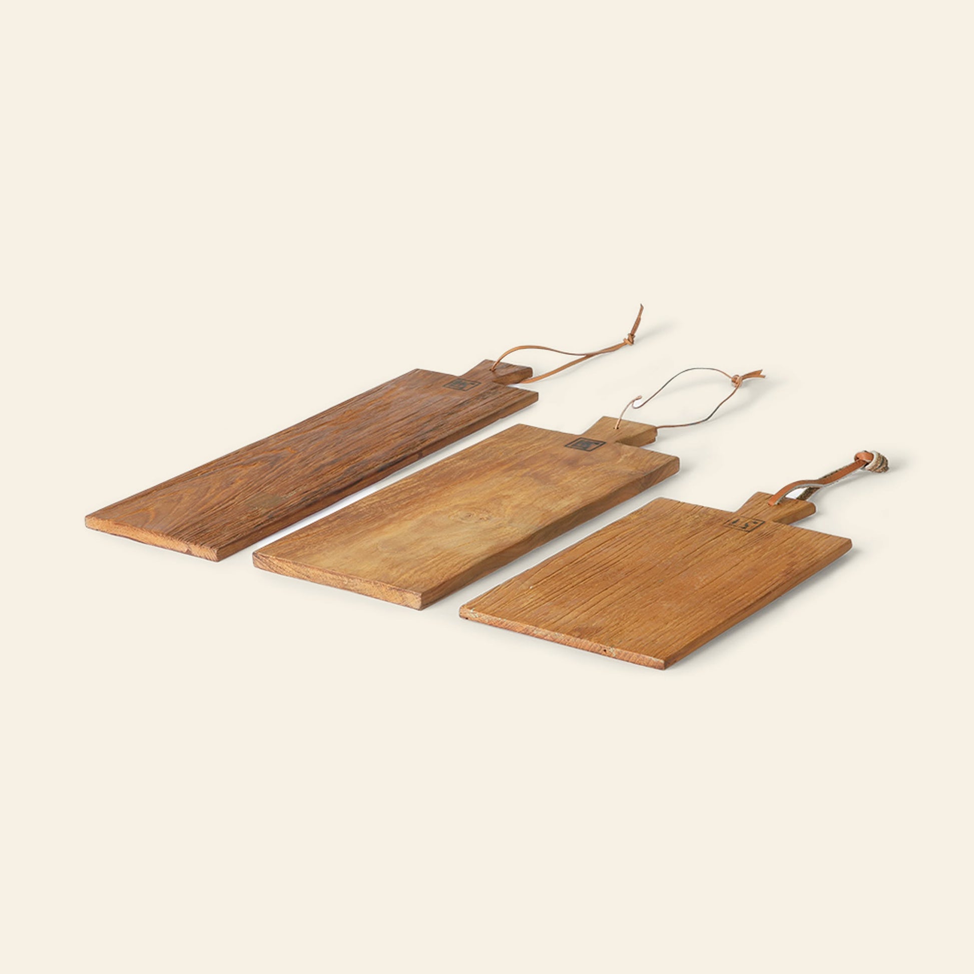 The HKliving Bread Board Teak, Set of 3 features rectangular teak boards in different sizes, each with a handle and leather loop for hanging—combining rustic charm and functionality. From the brand HKliving, shown side by side on a light background.