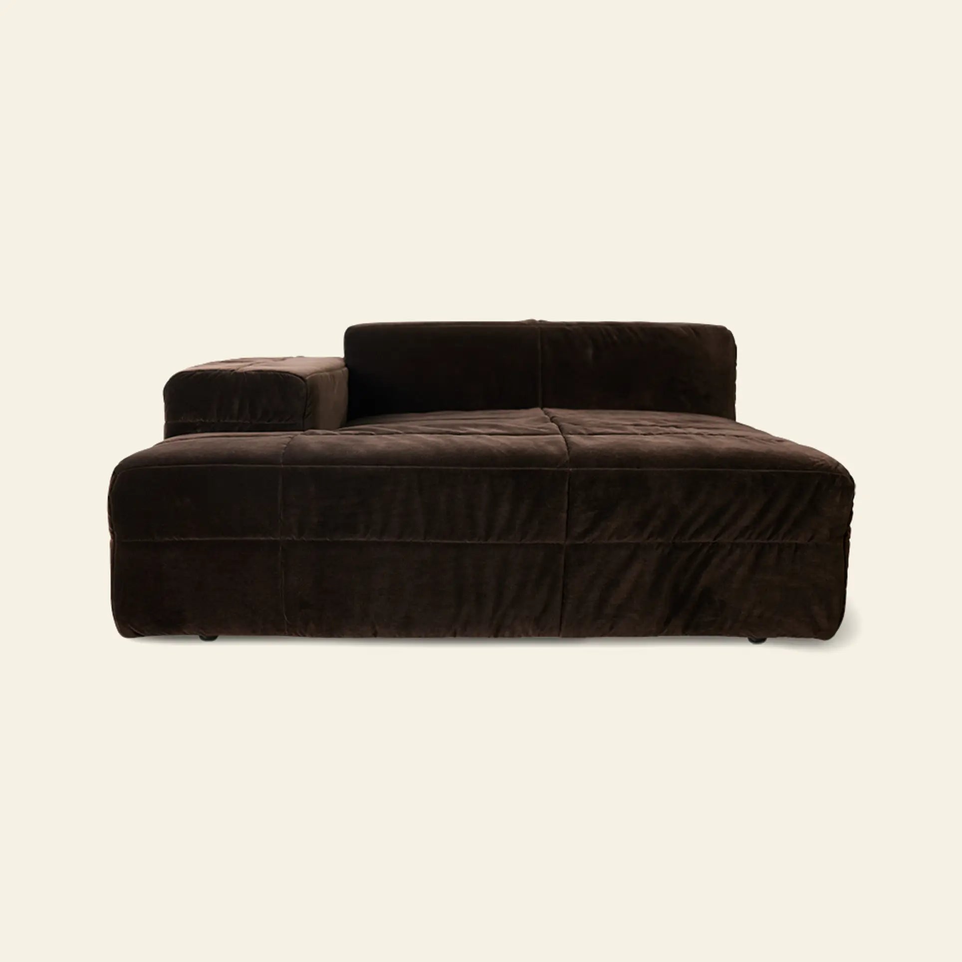 The HKliving Brut Sofa, Left by HKliving is a modern, low-profile chaise lounge in dark brown velvet with a bold brutalist shape, wide seat, and single left armrest, shown against an off-white background.