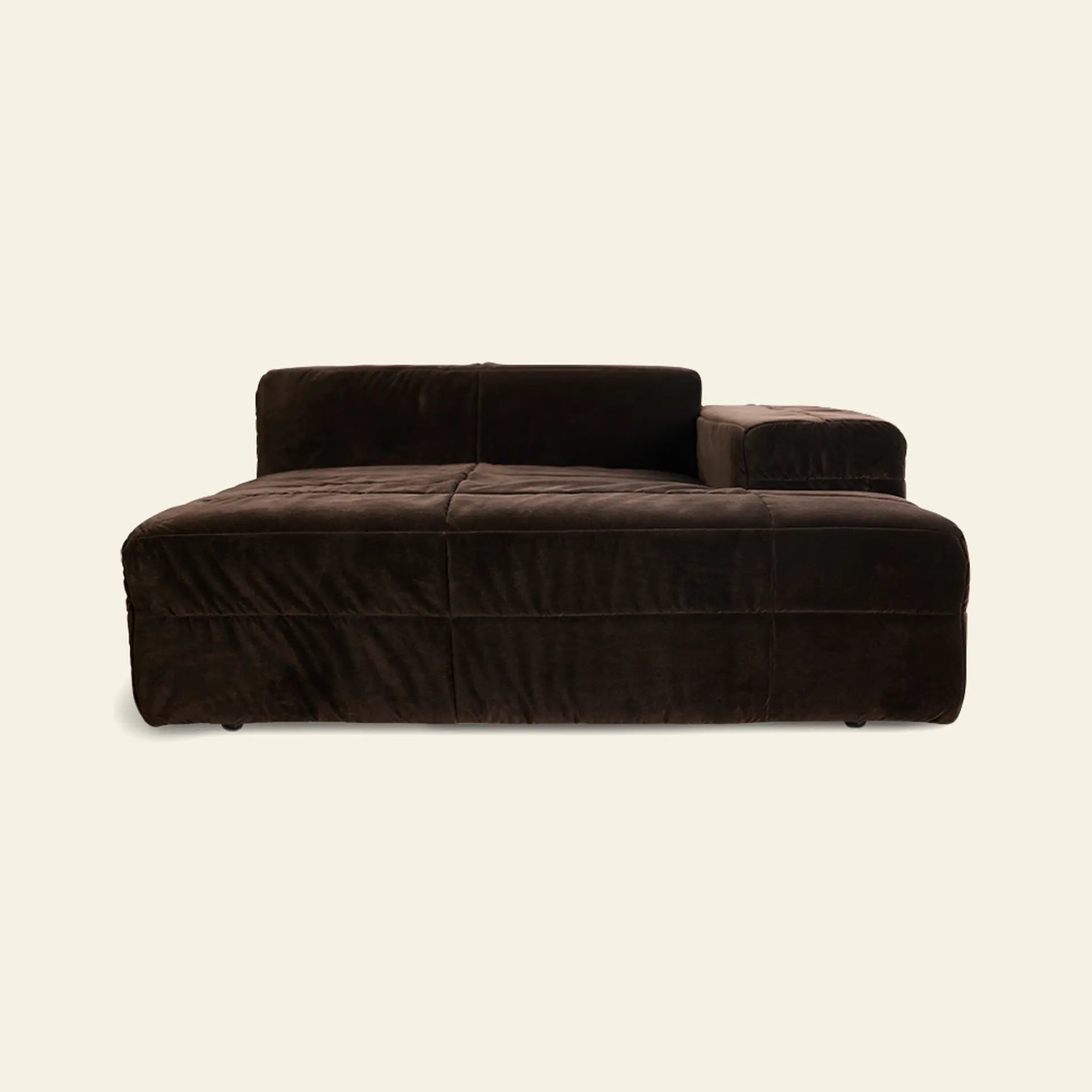The HKliving Brut Sofa, Right Divan by HKliving features a modern dark brown velvet design with a low backrest and wide armrest, providing spacious seating against a plain light beige background.