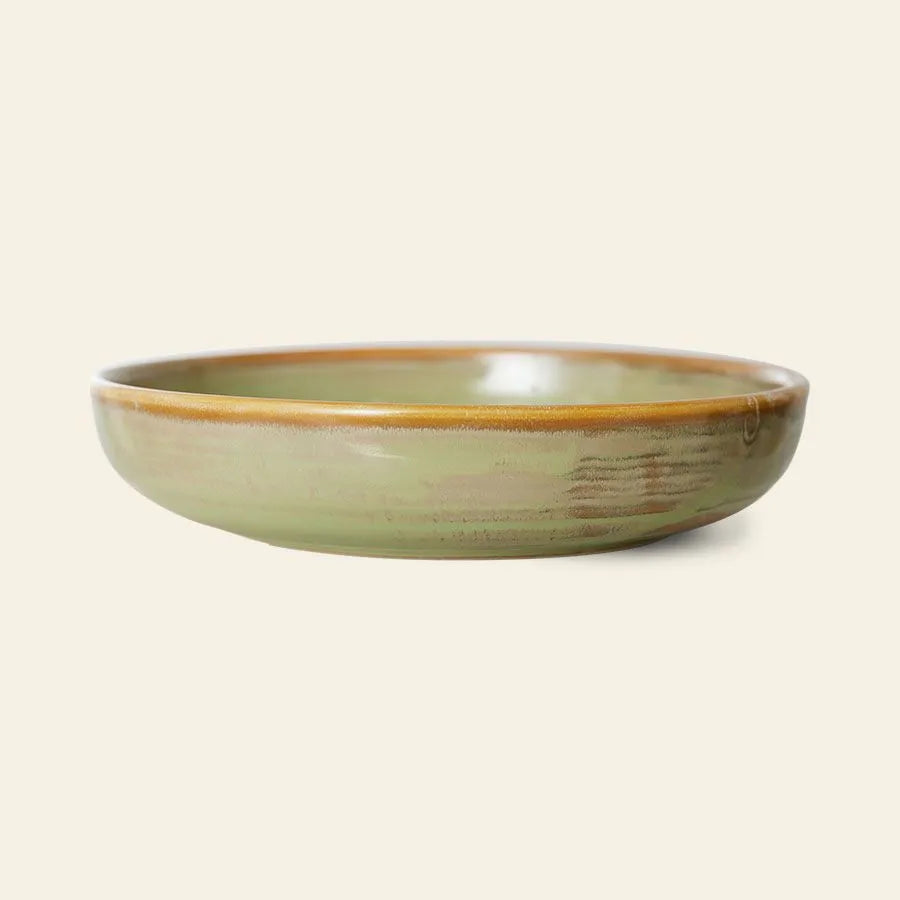 The HKliving Chef Ceramics: Deep Plate M by HKliving is a shallow, round ceramic plate with a smooth green reactive glaze and brown rim, exuding artisanal charm against a plain light beige background.
