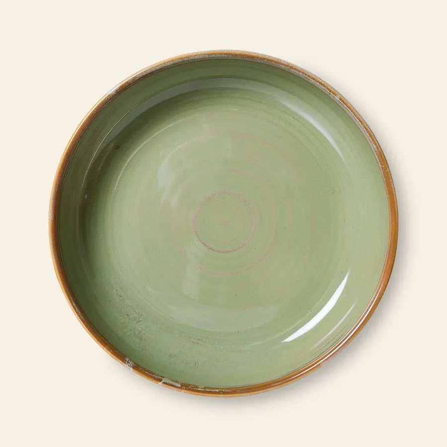 The HKliving Chef Ceramics: Deep Plate M is a round, shallow ceramic plate in glossy light green with a brown rim, exuding artisanal charm. Photographed from above against a cream background. Brand: HKliving.