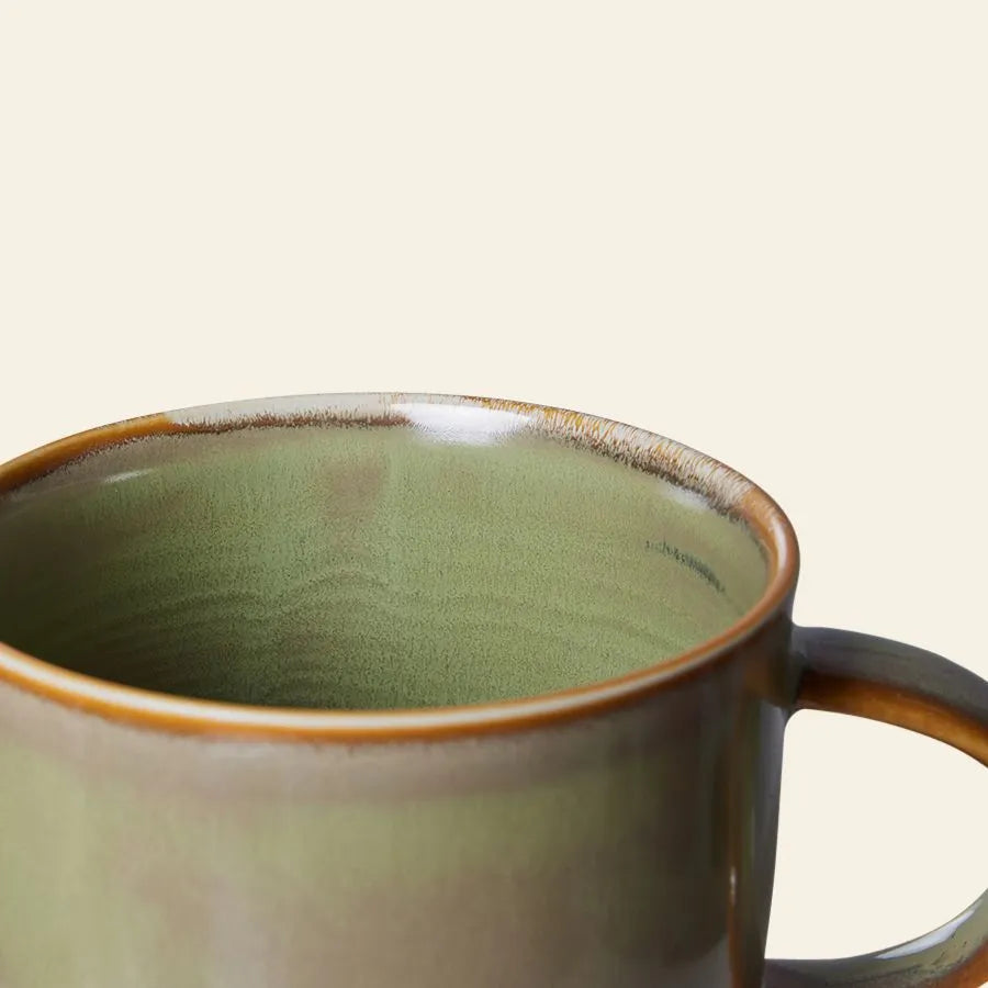A close-up of the HKliving Chef Ceramics: Mug by HKliving, featuring a green and brown glazed finish with artisanal charm on the upper half and handle, set against a plain cream background.