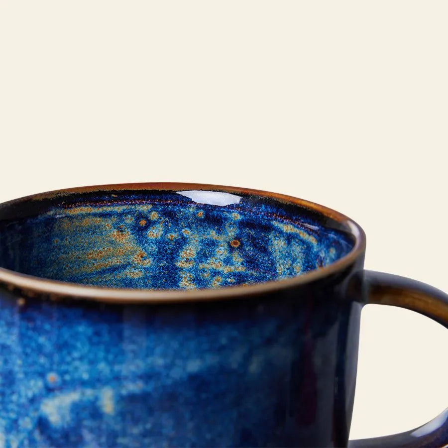 The HKliving Chef Ceramics: Mug by HKliving showcases artisanal charm with its rich blue and brown glaze, speckled design, and standout handle—an essential piece of tableware set against a plain light background.