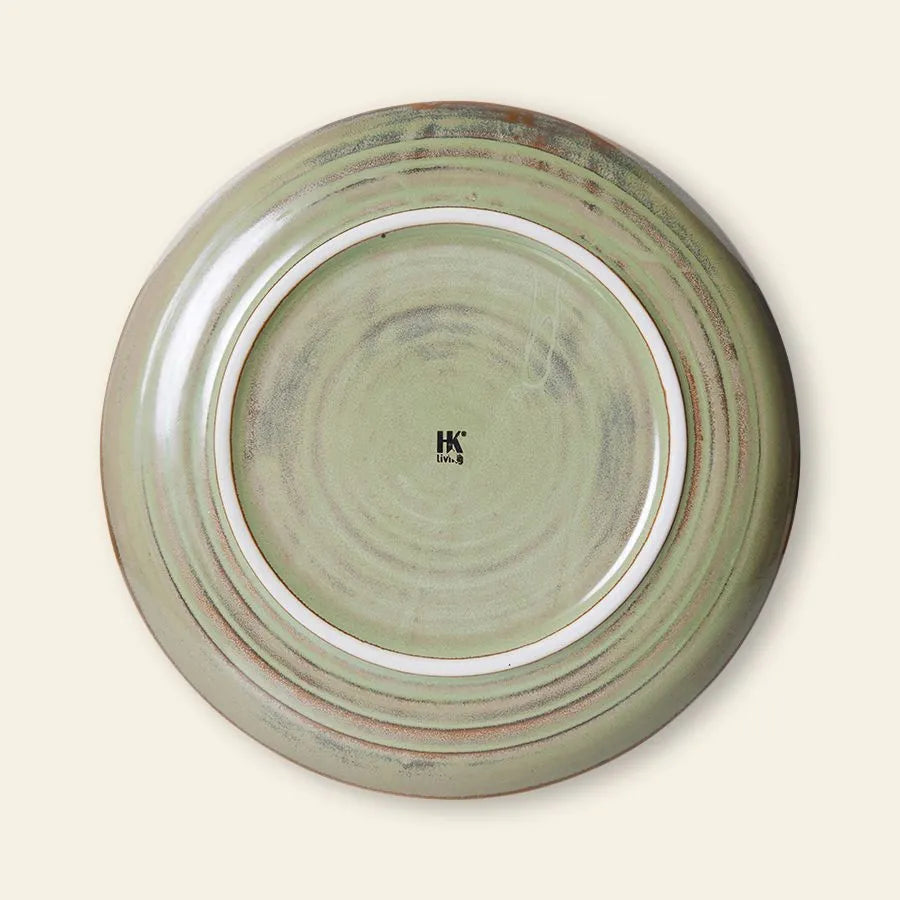 A round HKliving Chef Ceramics side plate with a greenish, slightly speckled reactive glaze is shown from the bottom. The center displays the black IK logo and India. It features a raised rim, subtle circular ridges, and artisanal craftsmanship.
