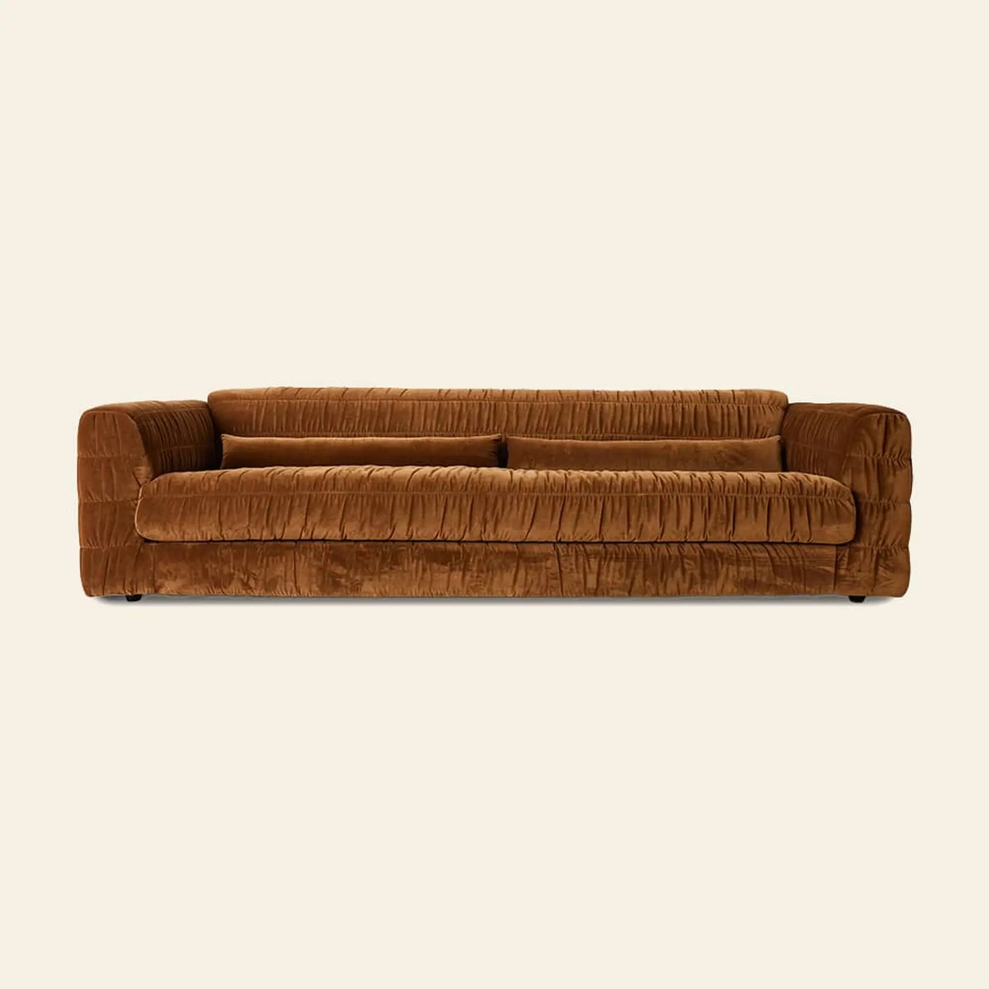 The HKliving Club Couch by HKliving is a modern, low-profile brown velvet sofa with plush pleated upholstery and wide armrests, offering exceptional seating comfort against a plain cream background.
