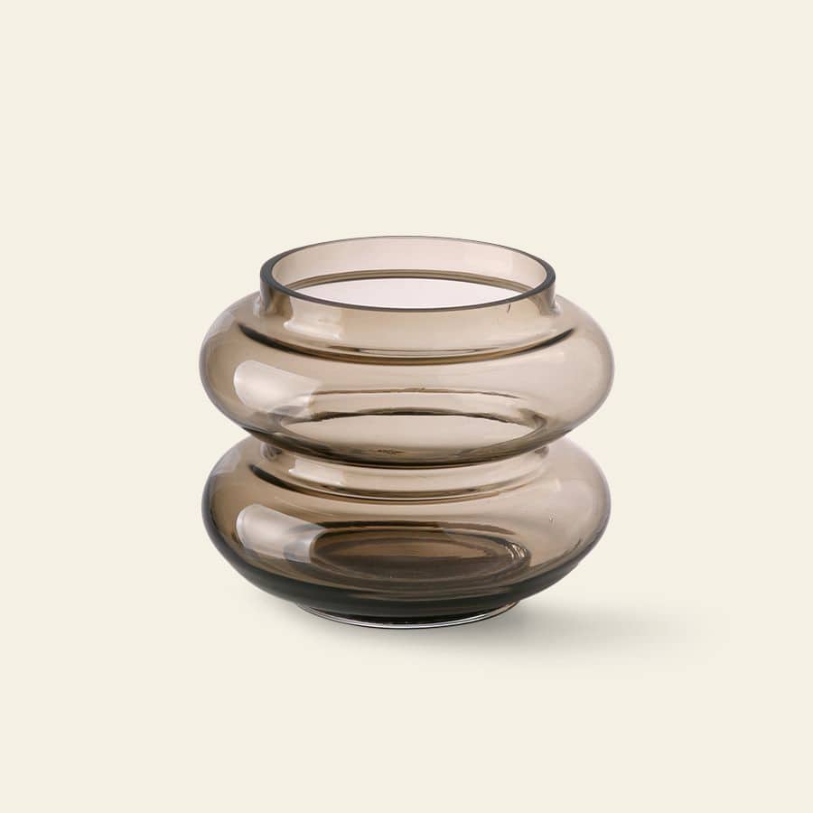 The HKliving Glass Vase S by HKliving, featuring a round, smoky brown glass design with a wide, wavy, and bulbous shape, brings minimalist elegance to your decor against a light beige backdrop.