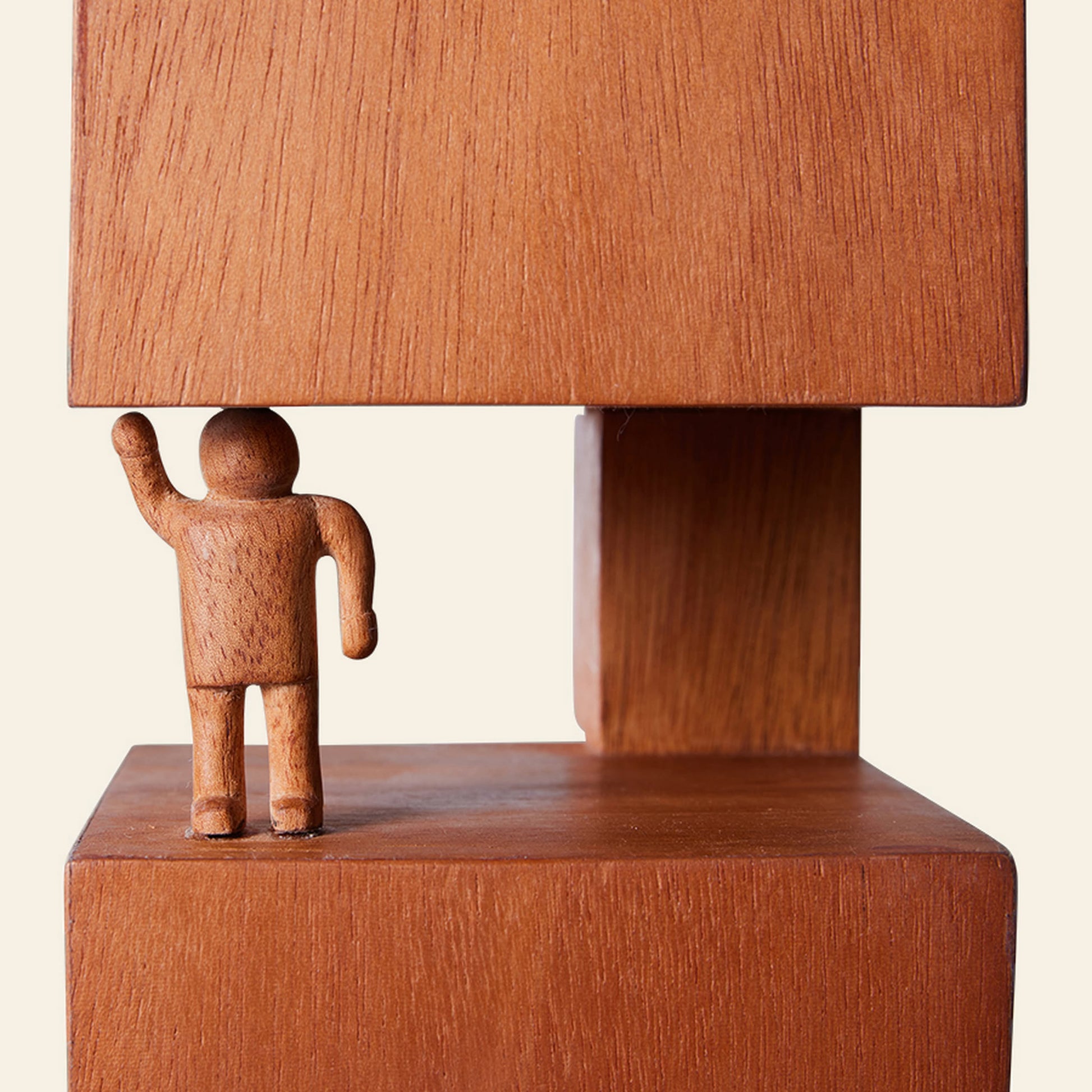 The HKliving HK Objects: Empowered is a small hand-carved figure with a raised arm, positioned between two large wooden blocks as if supporting the top one, creating an arrangement inspired by Bauhaus architecture.