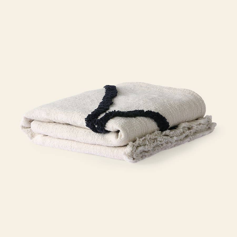 The HKliving Soft Woven Throw With Black Tufted Lines by HKliving, crafted from cosy cotton in cream with bold black tufted detailing, is neatly folded on a neutral beige background.