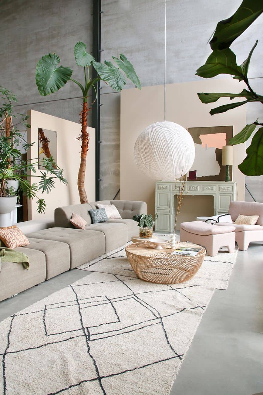 A modern living room with neutral furniture, leafy plants, a round wicker coffee table, geometric rug, cosy HKliving Soft Woven Throw With Black Tufted Lines for texture, pale green sideboard, white pendant light, high ceilings, and soft natural light.