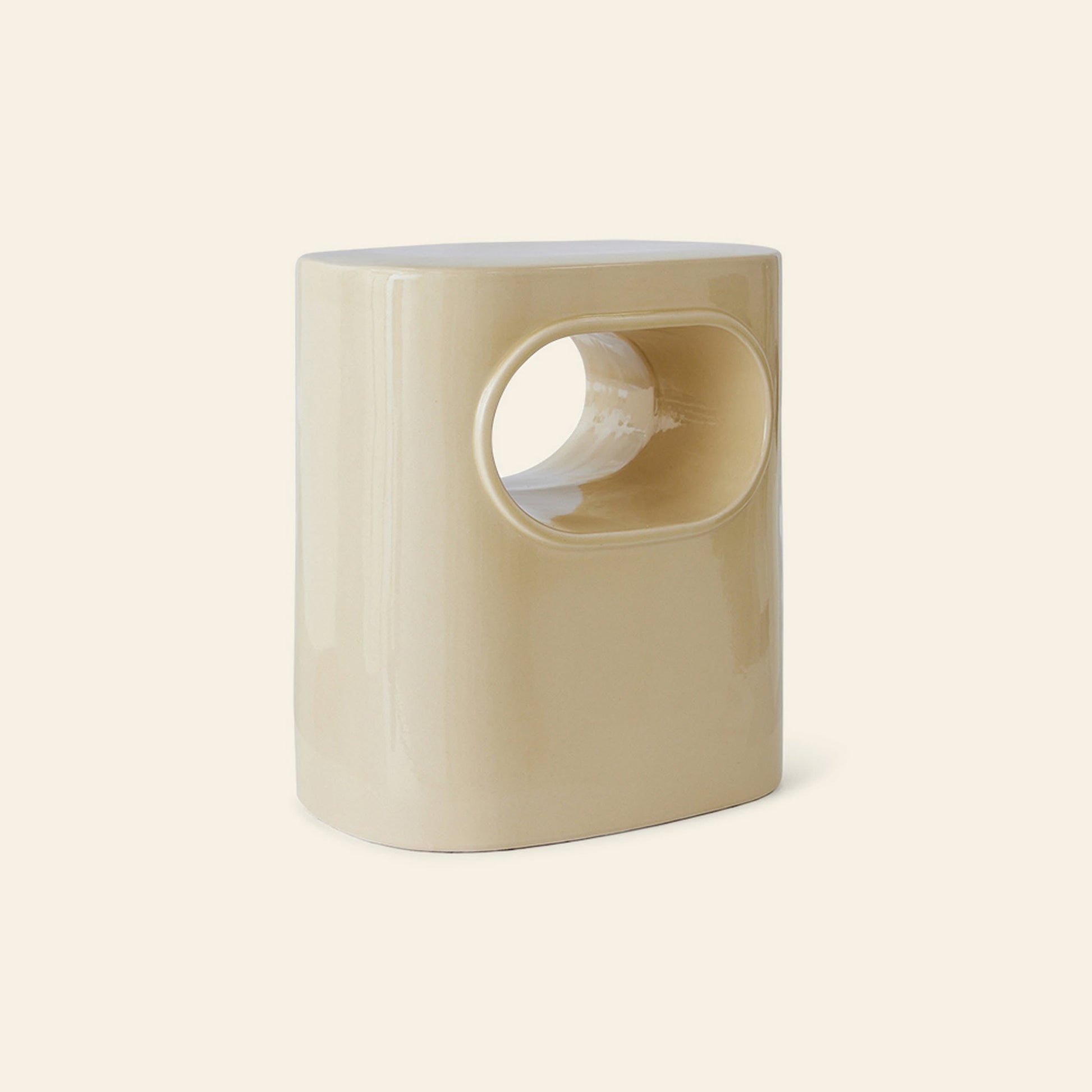 The HKliving Space Side Table by HKliving is a glossy, oval-shaped beige ceramic stool with a central rounded rectangular cutout, offering modern design and multifunctionality as a side table, shown on a plain light background.