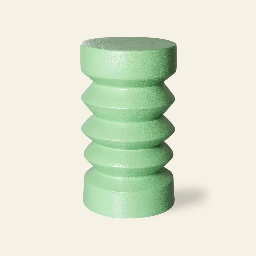 The HKliving Stoneware Side Table by HKliving is a light green, cylindrical accent crafted from durable stoneware with a sculpted geometric design of alternating ridges and grooves, shown against a plain beige background.