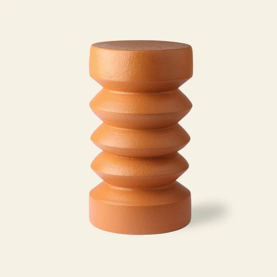 The HKliving Stoneware Side Table by HKliving, featuring a cylindrical, terracotta-colored design with four rounded ridges and flat surfaces, adds a whimsical charm to any space against a light background.