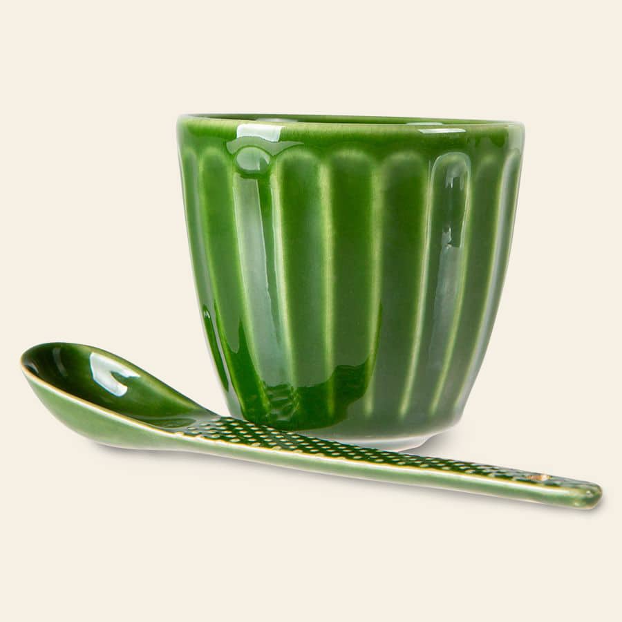 The HKliving The Emeralds: Ceramic Mug Ribbed, Set of 4 features green ceramic mugs with a ribbed design, shown beside a matching spoon on a light beige background.