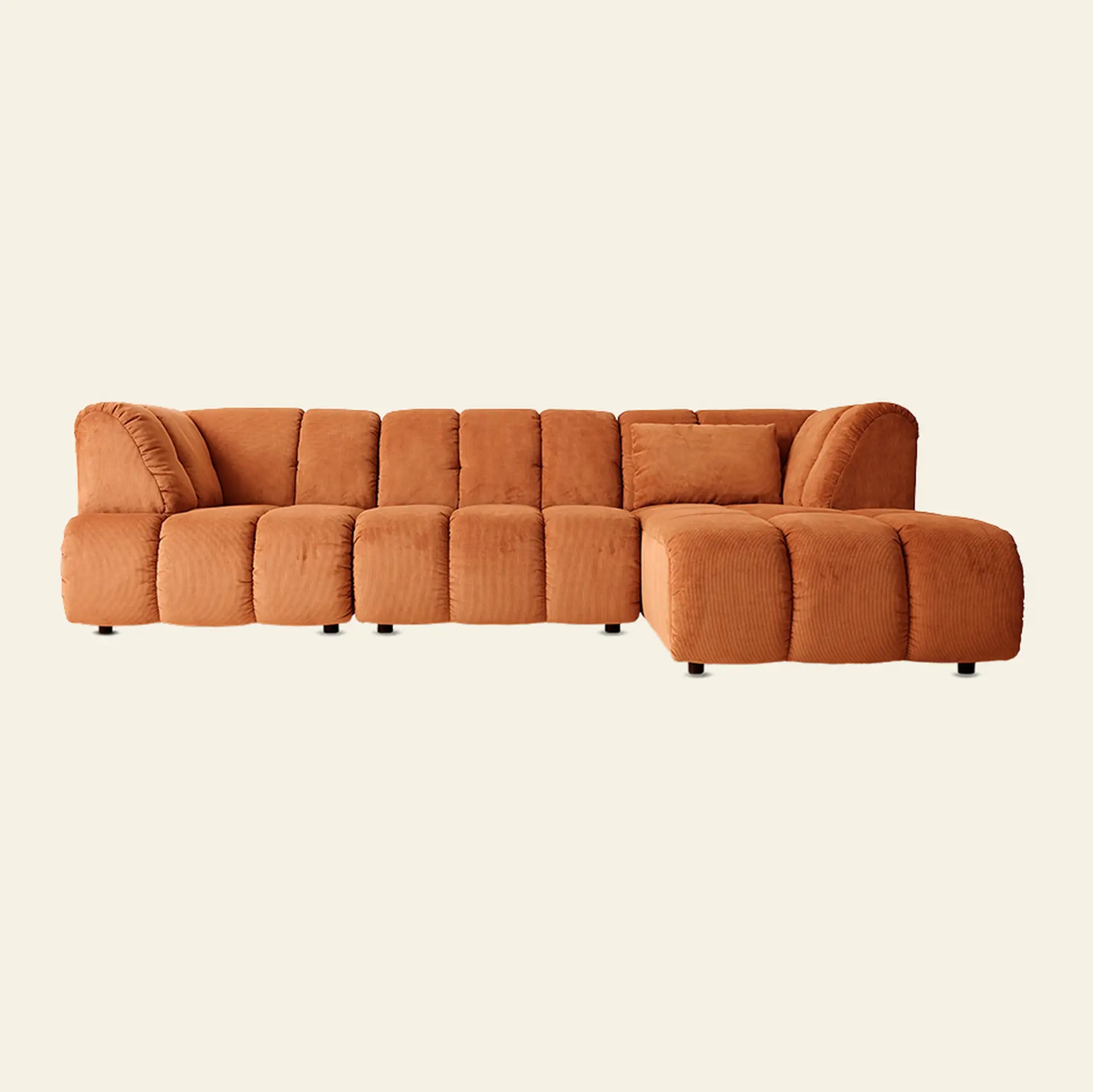 The HKliving Wave Couch, Corner by HKliving is an L-shaped modern sofa in warm orange with plush ribbed upholstery and low black legs, creating a standout piece of living room furniture against a light background.