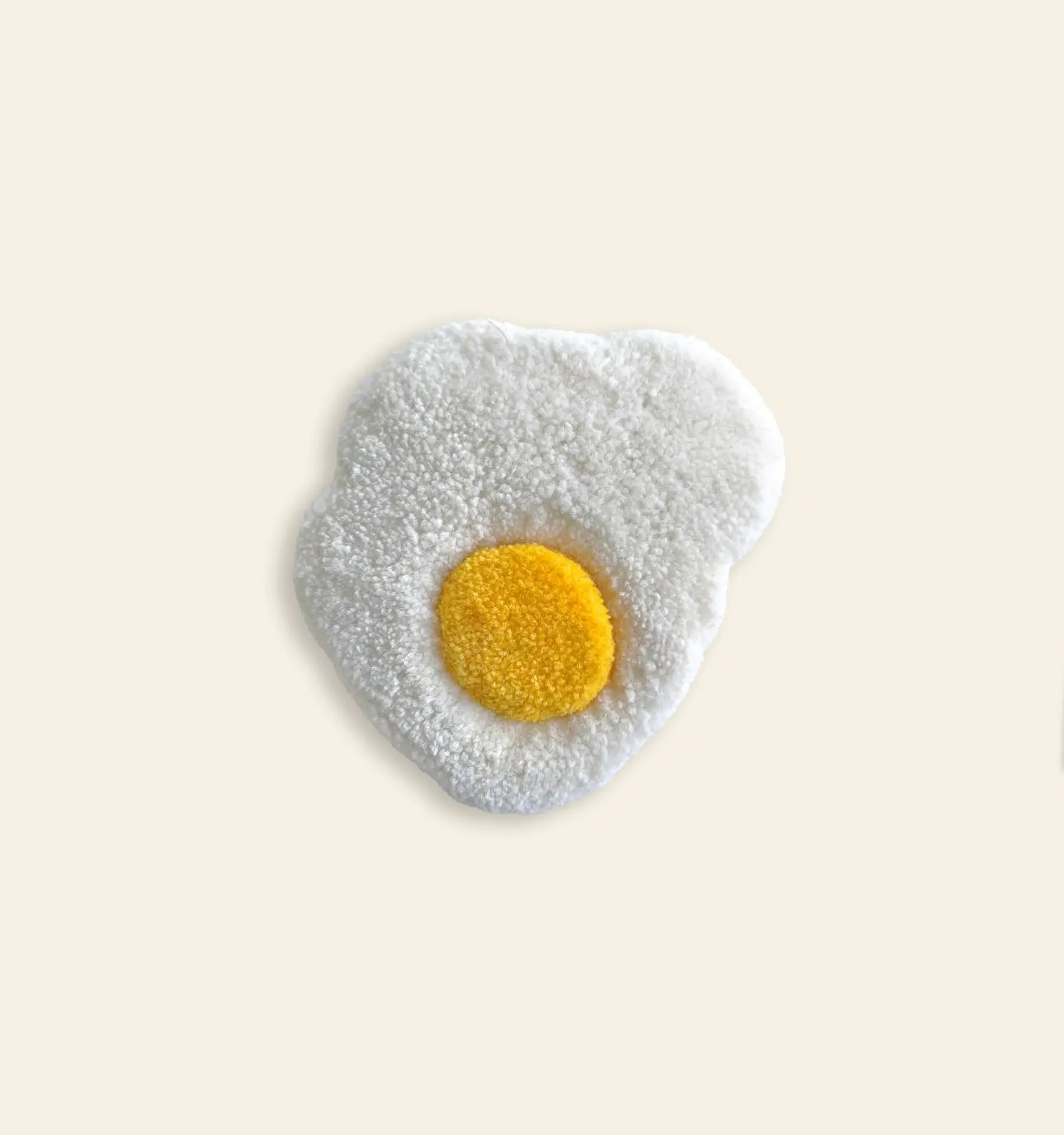 The Habichl Tufted Egg Coasters by Habichl feature a soft, textured design with a yellow center and a white squiggly border, resembling sunny-side-up eggs, displayed on a light beige background.