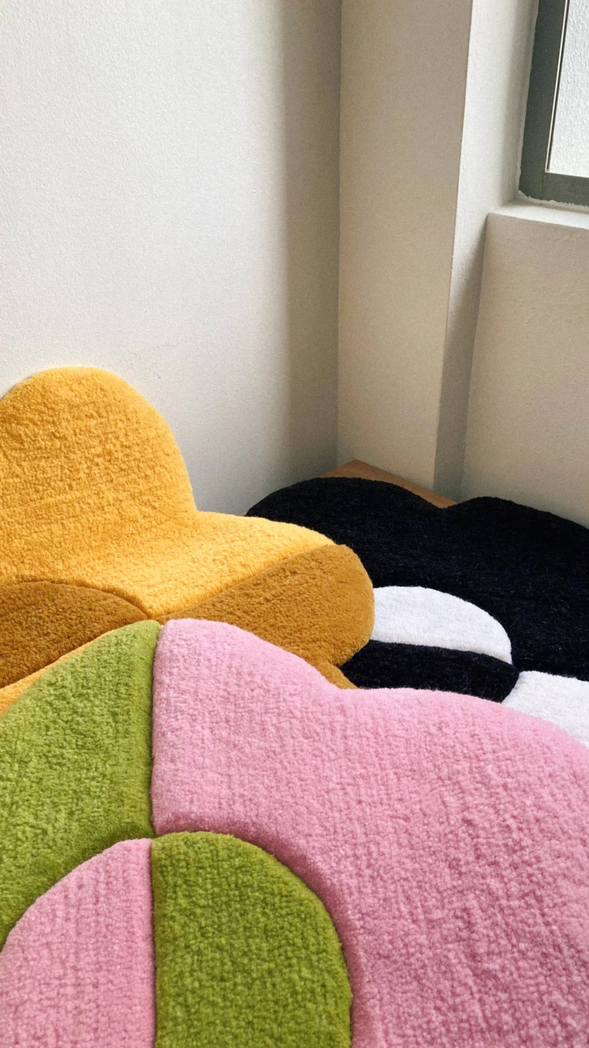 Three Habichl Tufted Flower Floor Rugs from Habichl—in yellow, pink and green, and black and white—add a whimsical touch to a bright room when arranged by the window.