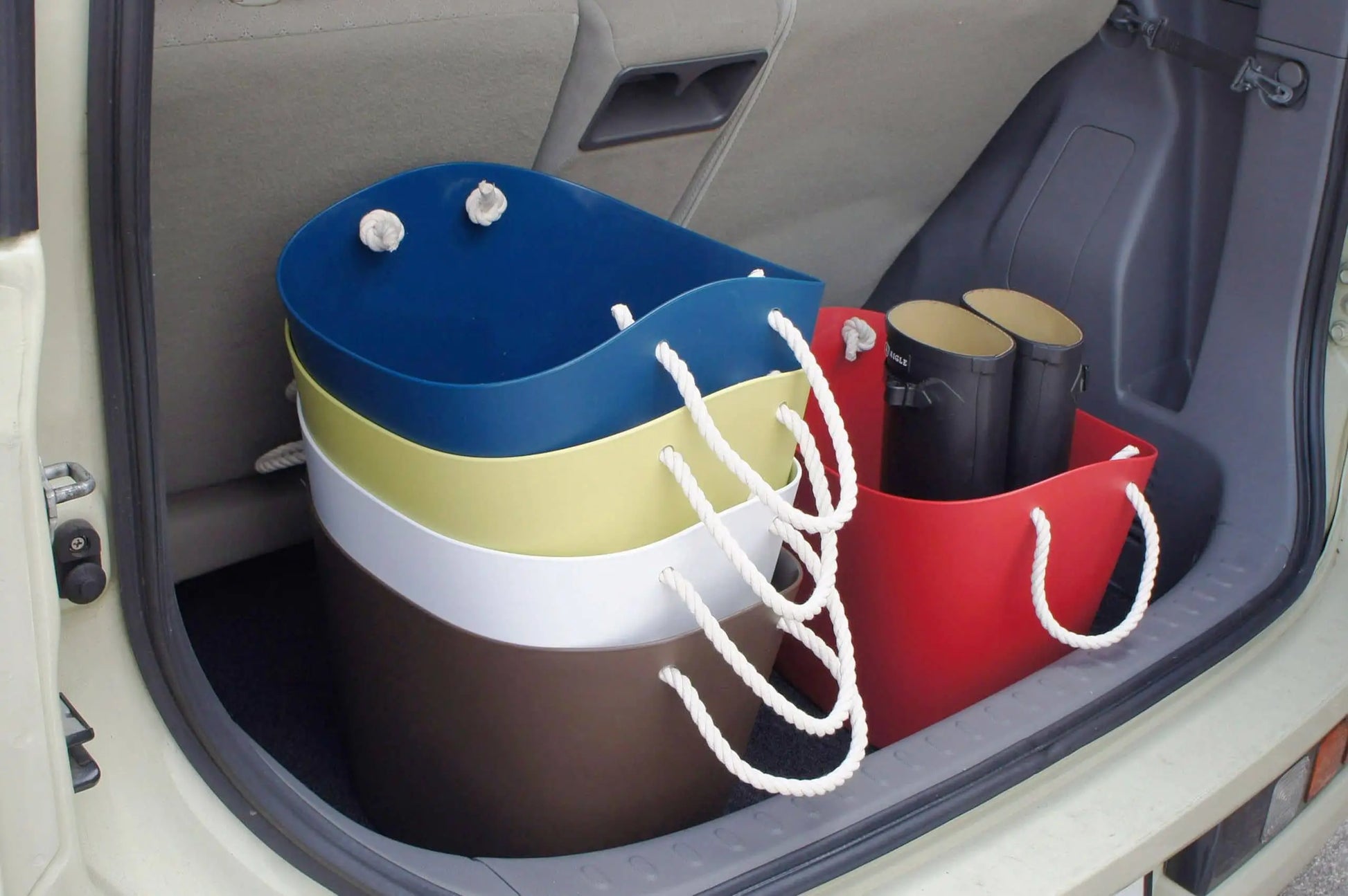 Four colorful Hachiman Balcolore Storage Basket M pieces with rope handles and a red tote holding black tubes are neatly arranged in a car trunk, reflecting minimalist Japanese style and versatile storage by Hachiman.