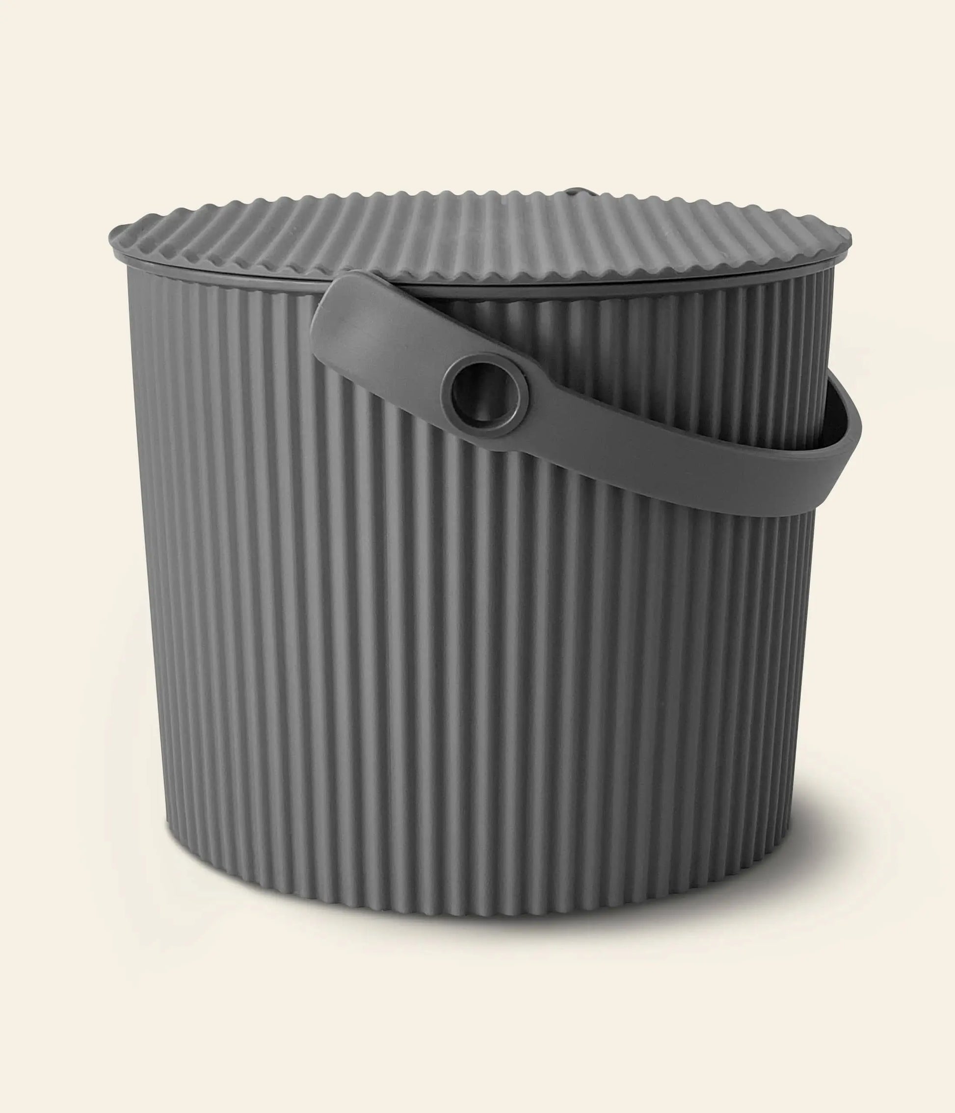 The Hachiman Omnioutil Storage Bucket S by Hachiman is a round, dark gray bucket with a ribbed lid and flexible handle, ideal for indoor or outdoor use. Its shown against a plain light background.