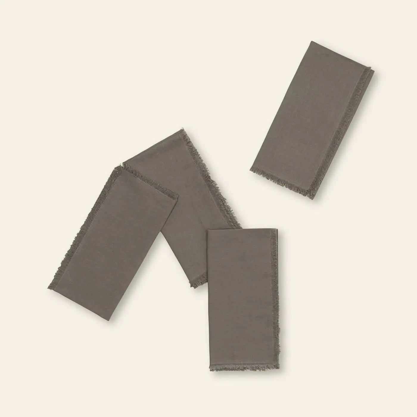 The Hawkins New York Essential Dinner Napkins, Set of 4, are elegantly styled with frayed edges and displayed on a light beige background—two flat, two folded—for a refined table setting.