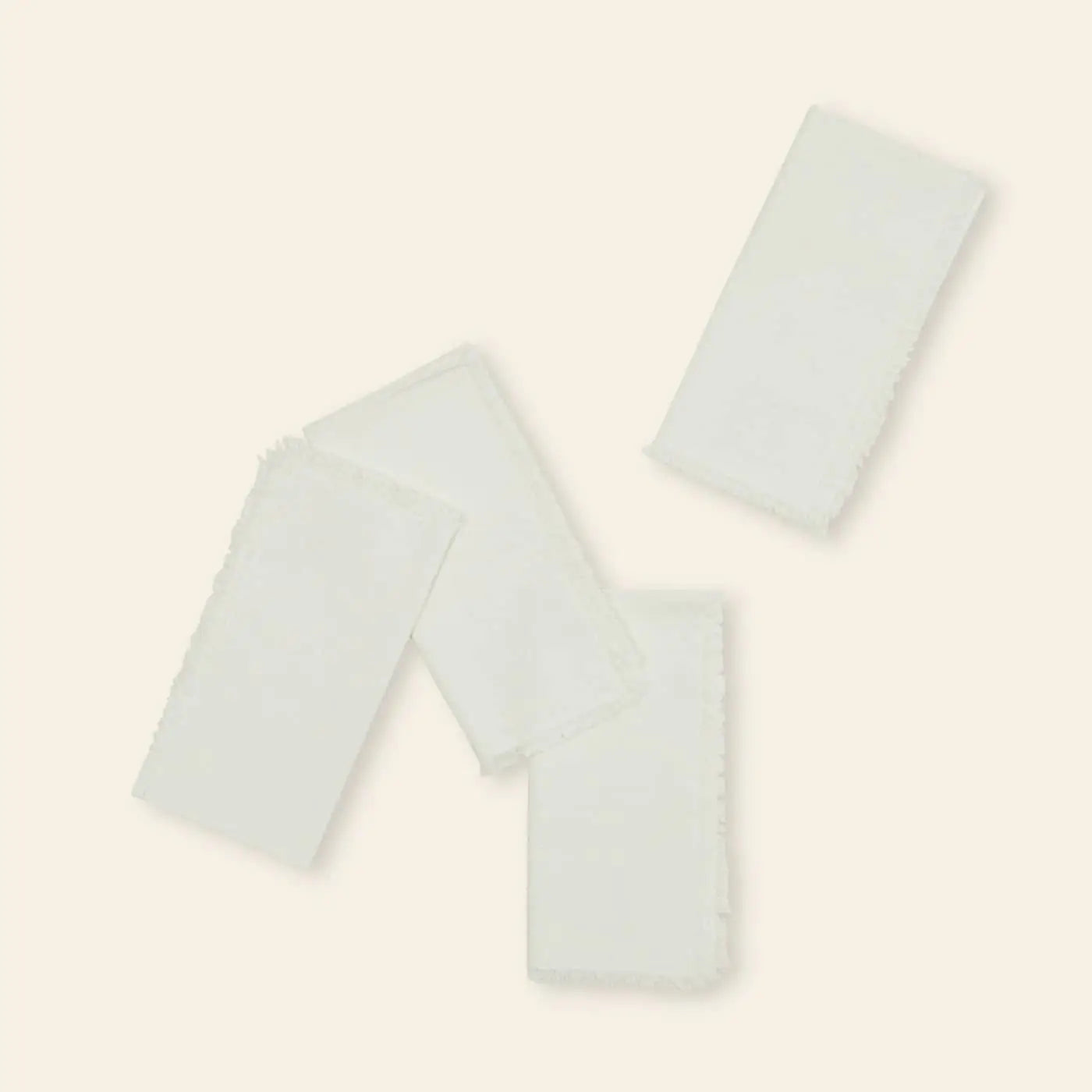 A set of four white Hawkins New York Essential Dinner Napkins is arranged at varied angles on a light beige background—an elegant way to elevate your table setting.