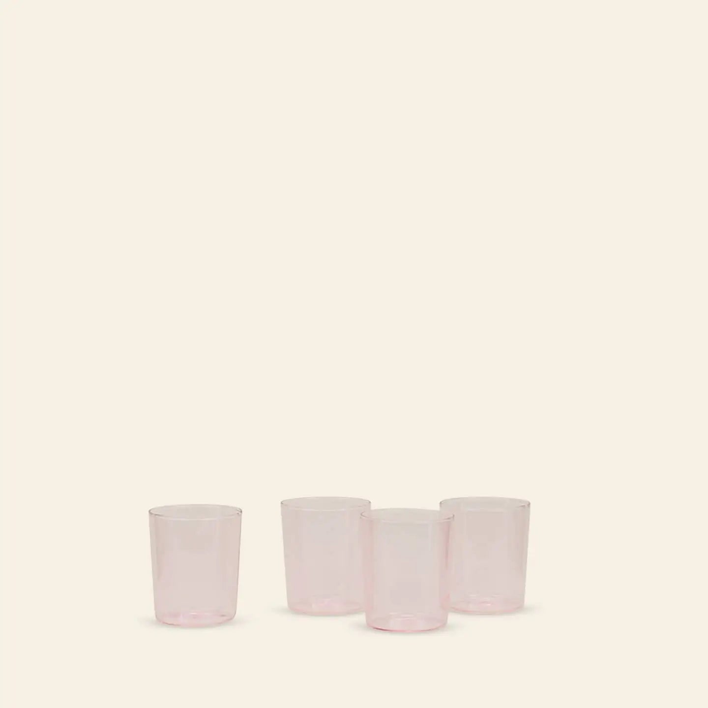 A set of four translucent pink Hawkins New York Essential Glassware (Medium) is arranged in a row on a light beige background—three grouped, one set apart—showcasing the brand’s premium quality.