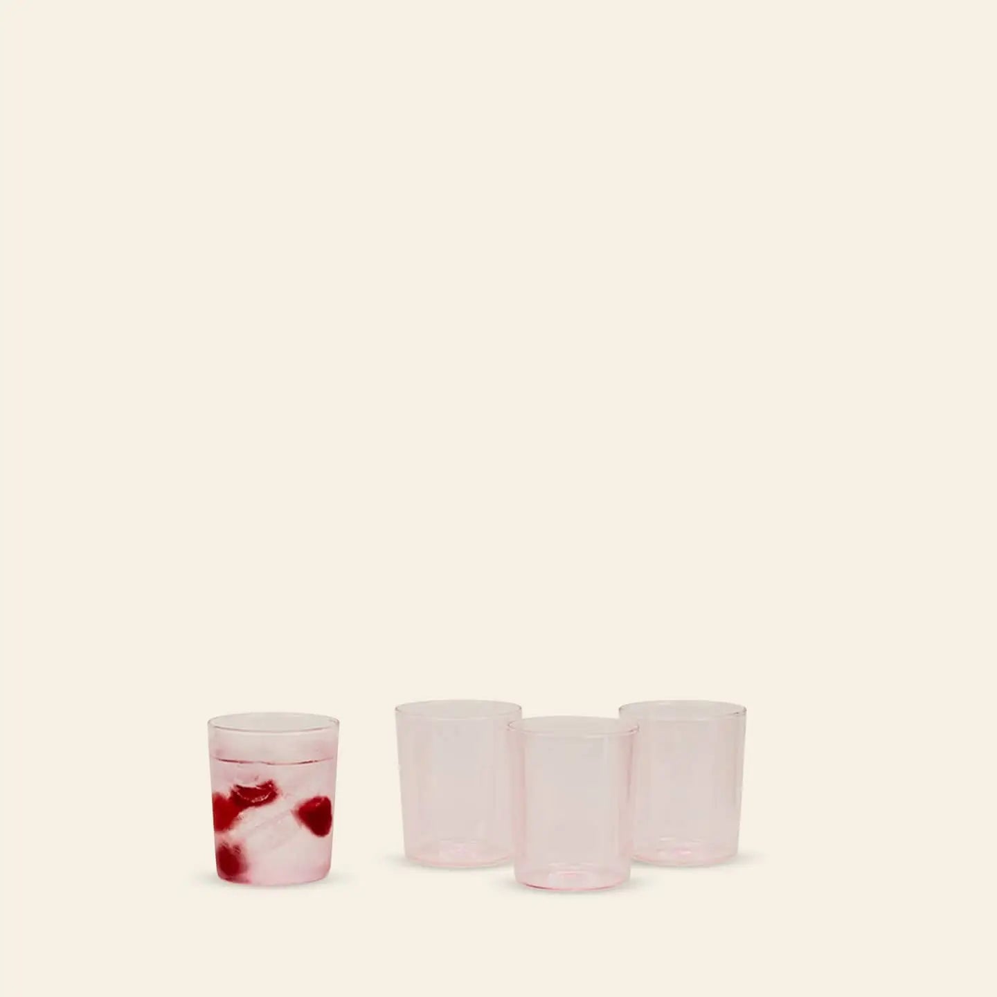 Four translucent pink Hawkins New York Essential Glassware, Set Of 4, Medium are displayed on a plain background—three empty and one filled with ice and two red cherries—highlighting their premium quality for any occasion.